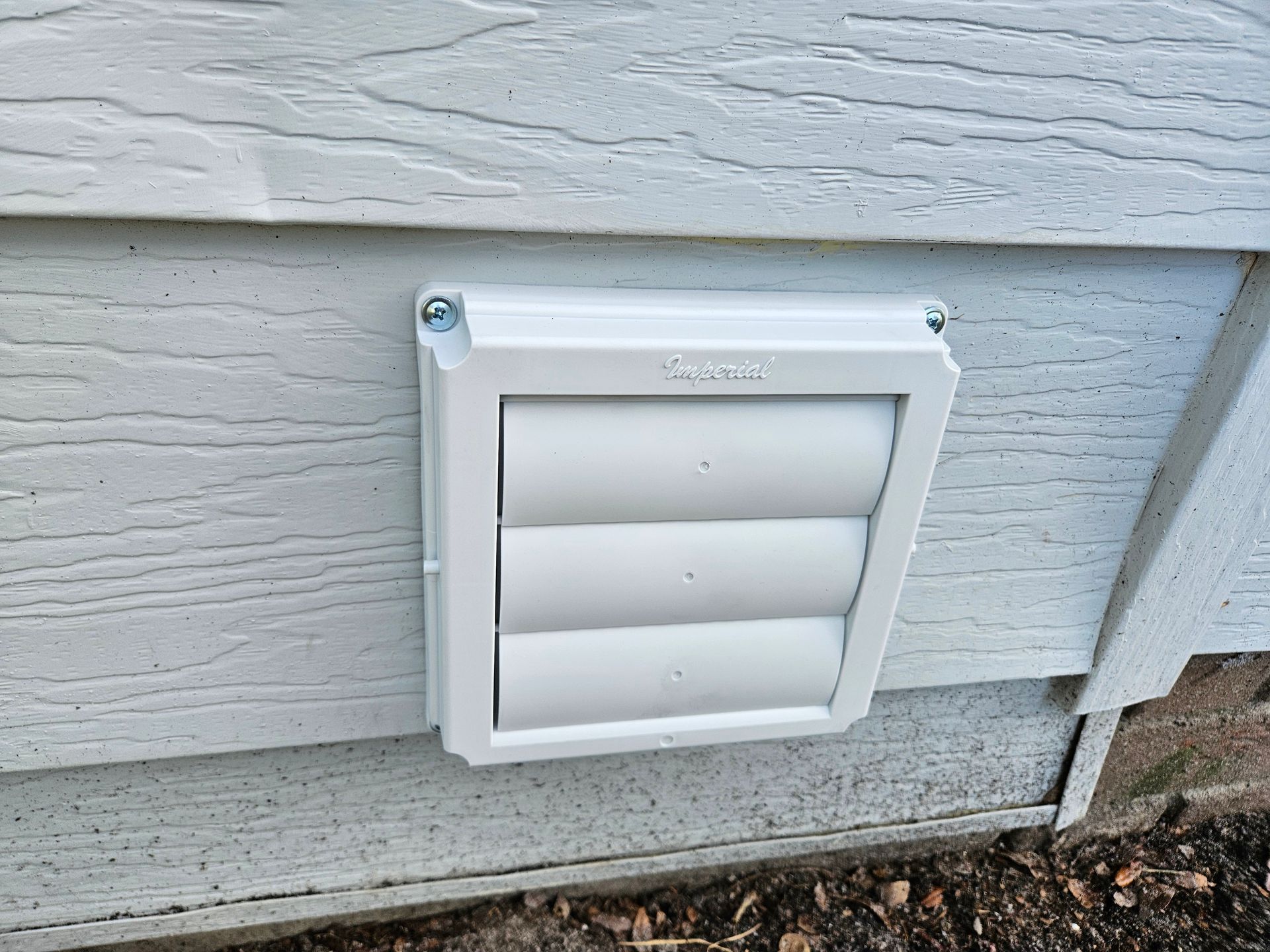 White dryer vent on a gray siding wall, with horizontal louvers.
