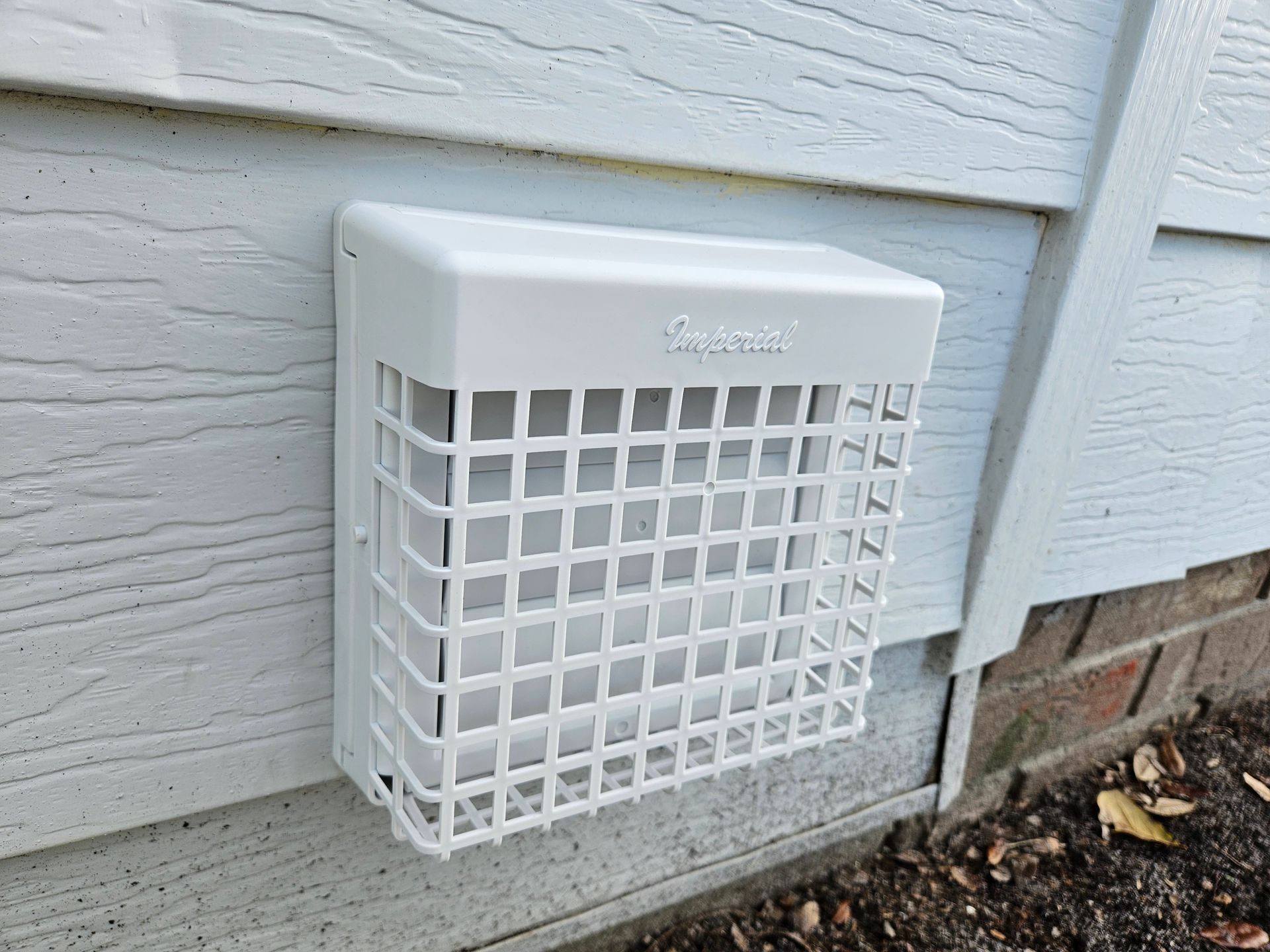 White plastic vent cover on a house's siding, protecting a dryer or exhaust vent.