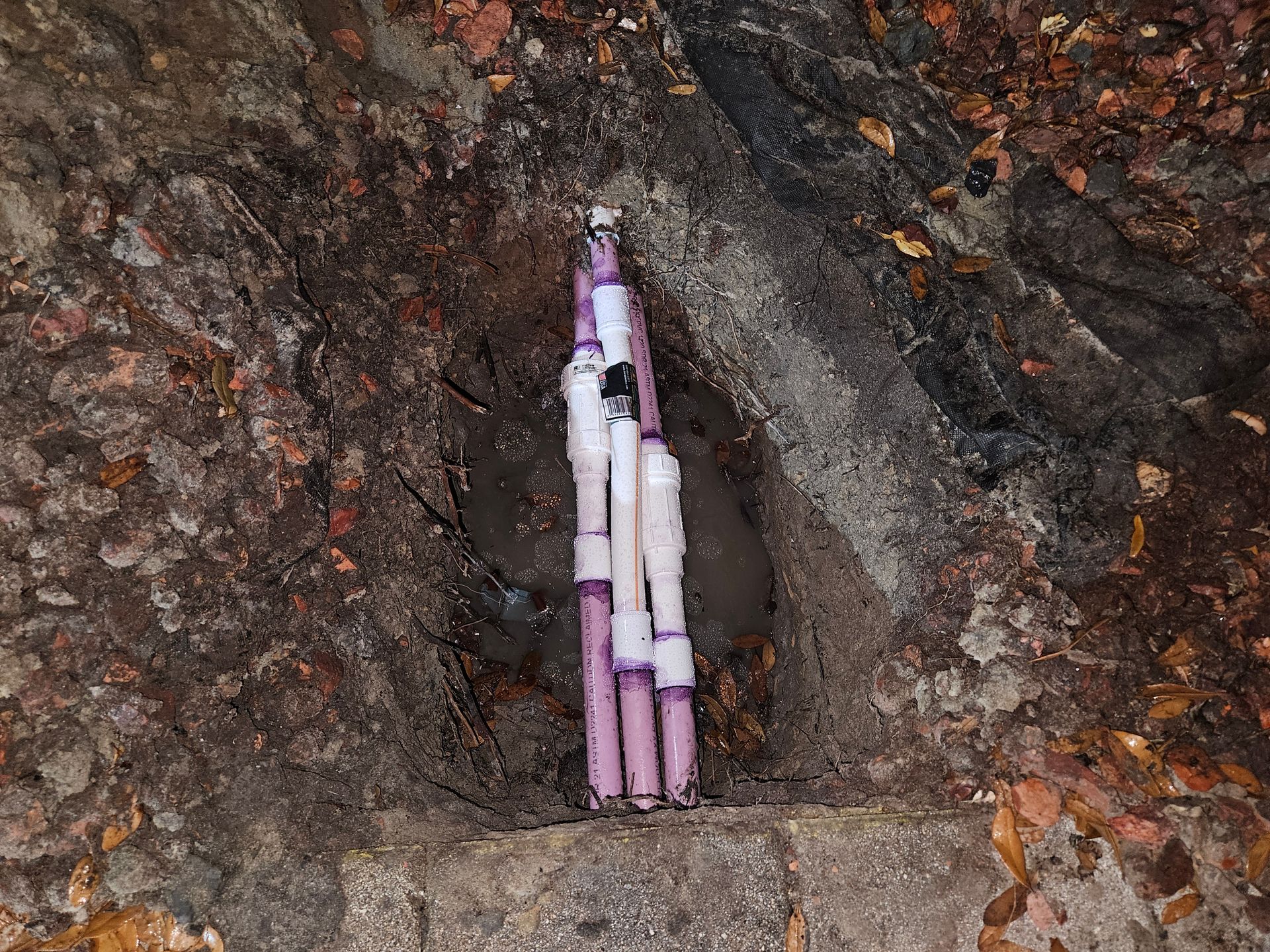 Purple and white PVC pipes within a dark hole in a reddish-brown earthen wall.