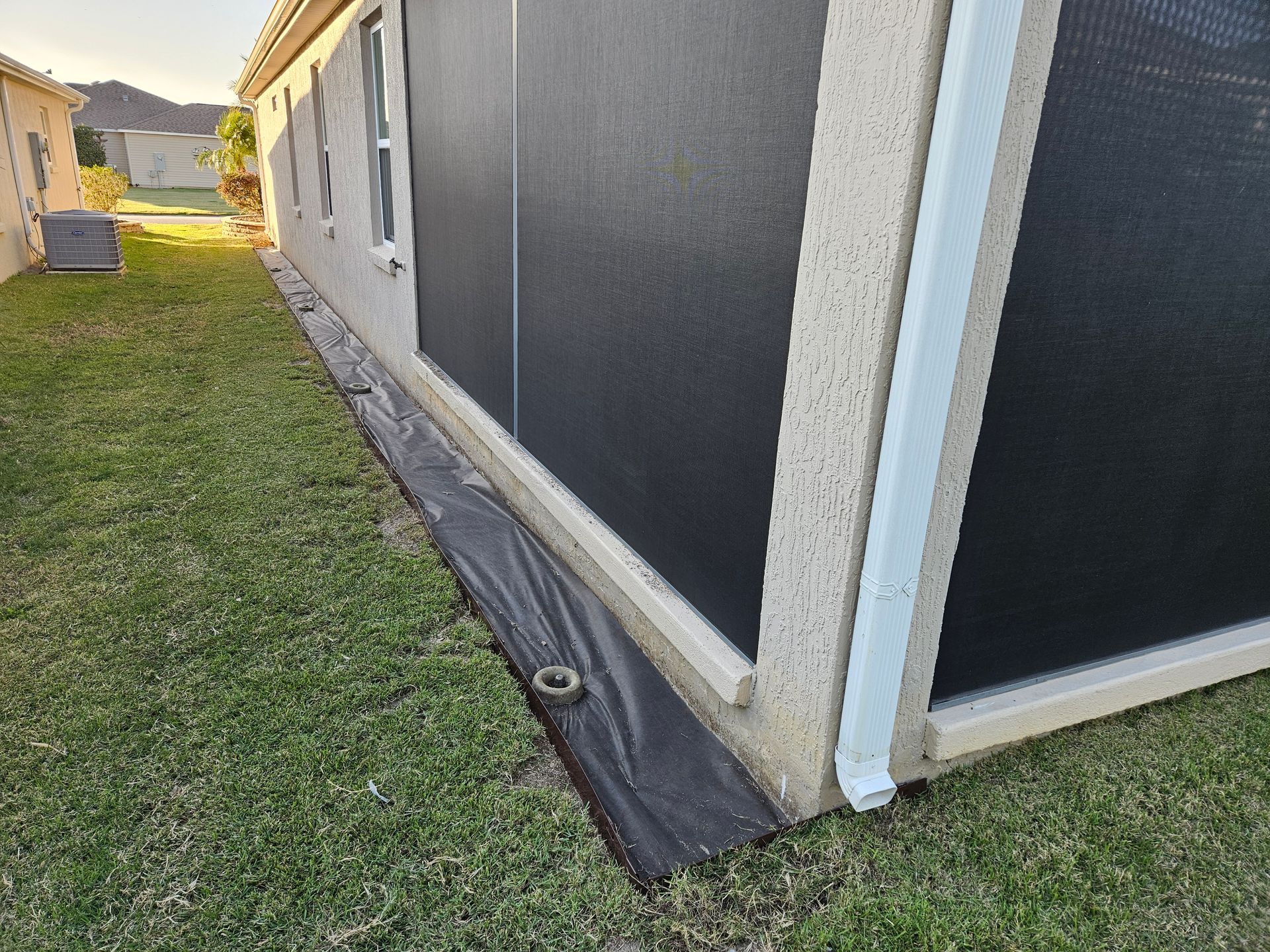Exterior of a house with black mesh screens. Black fabric lies on the ground next to the building, grass in the foreground.