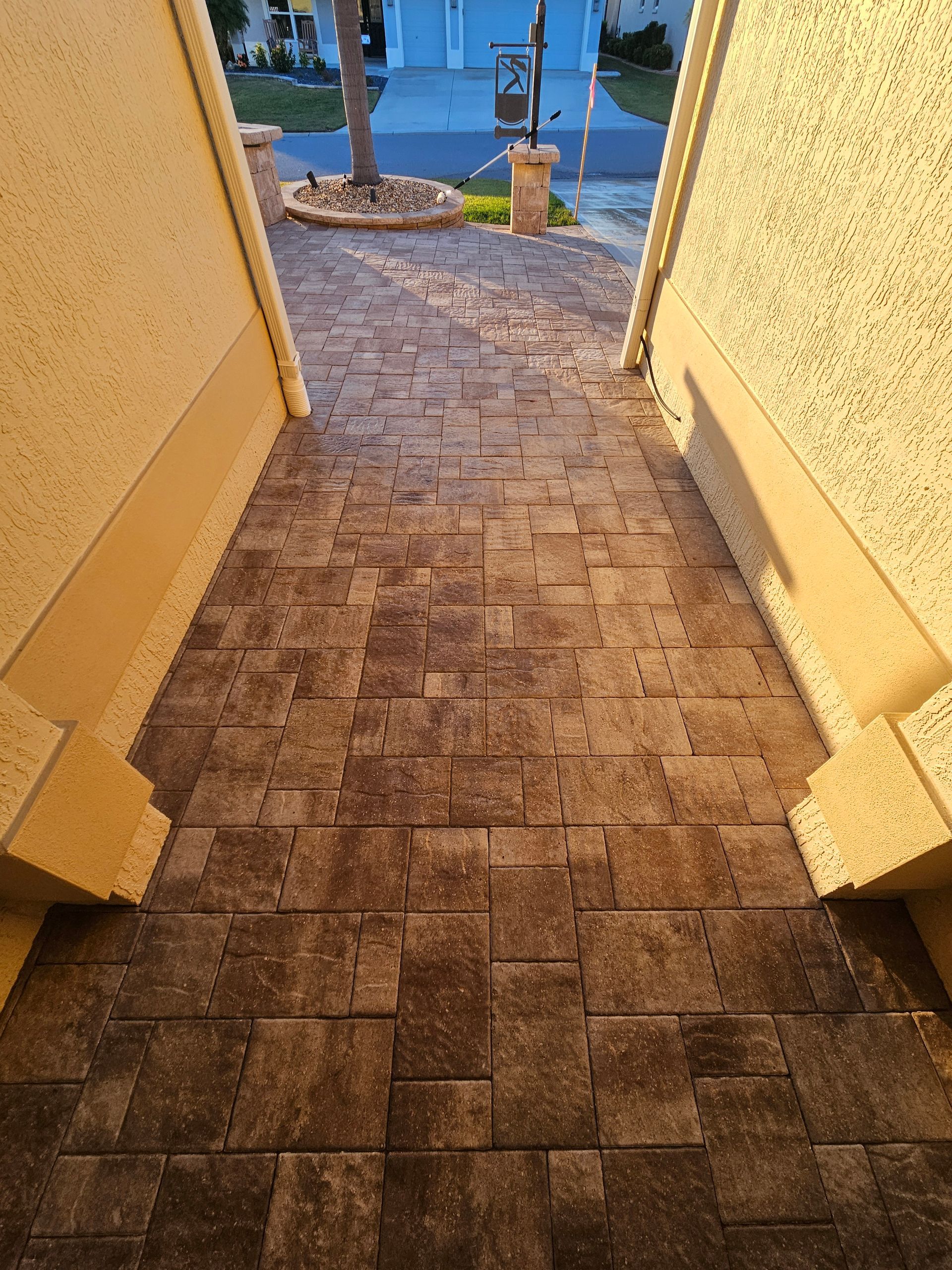 Brick walkway leading towards the street, framed by beige walls, outside.