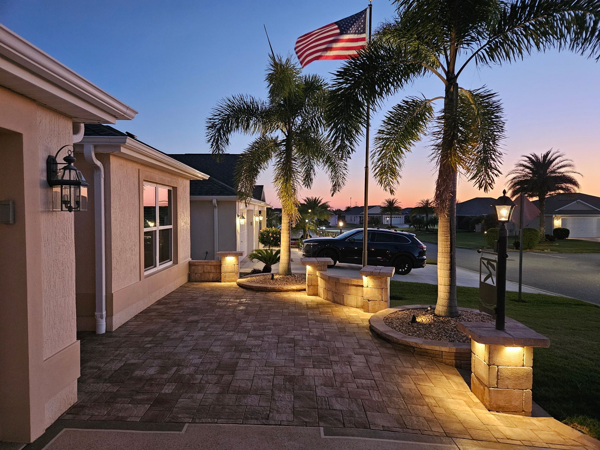 Brick patio lit by lamps at dusk with palm trees and American flag.