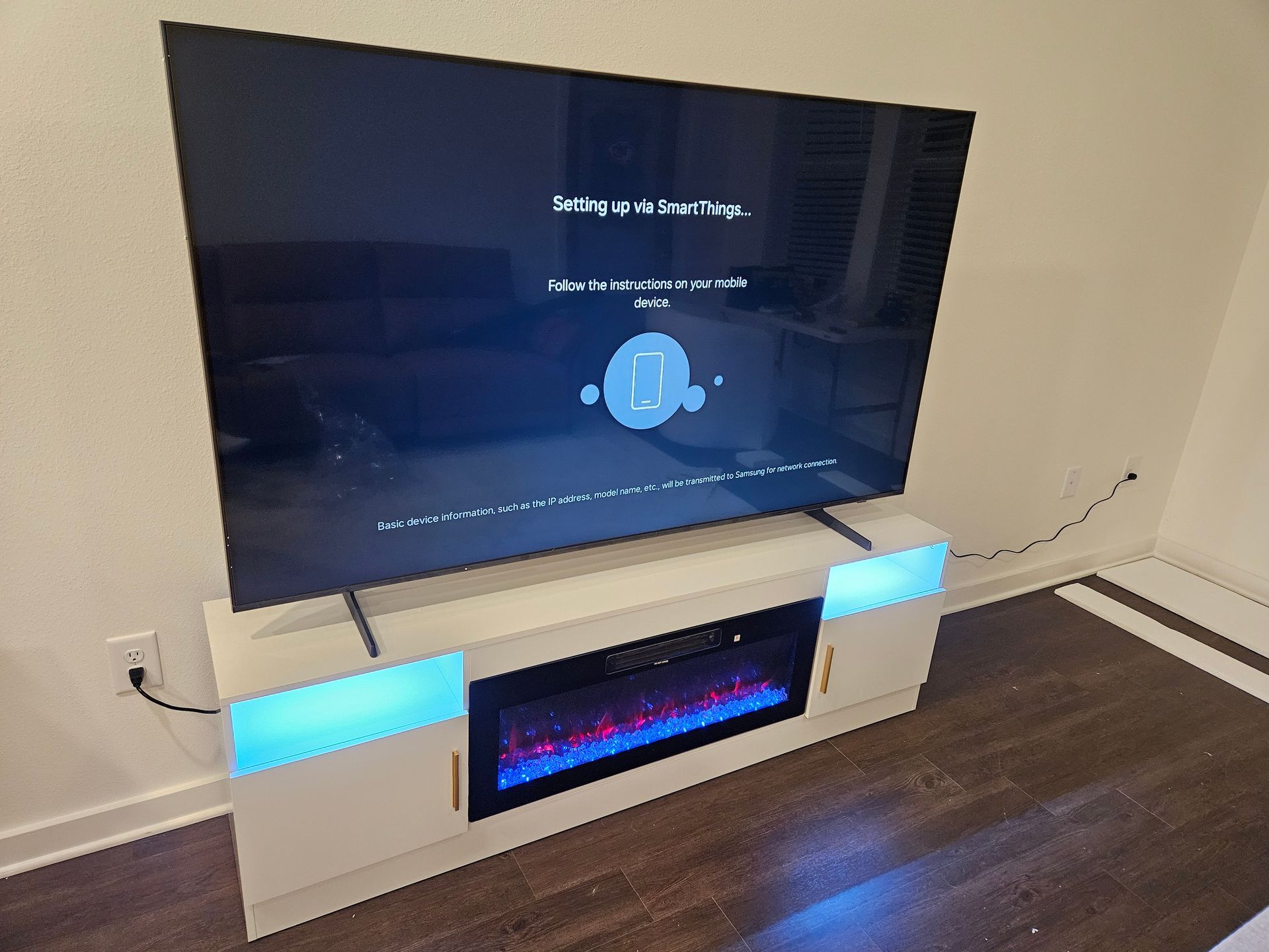 TV screen displaying setup instructions atop a white entertainment center with a built-in fireplace and color-changing lights.