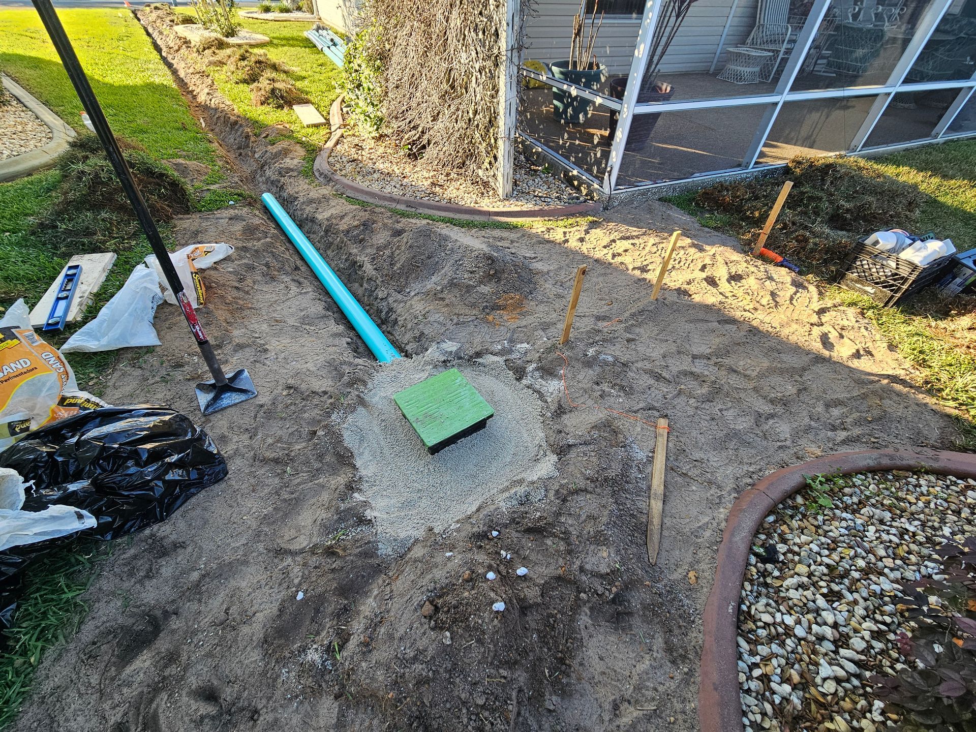 Construction site with a blue pipe, concrete base, and dirt path; near a screen enclosure and lawn.