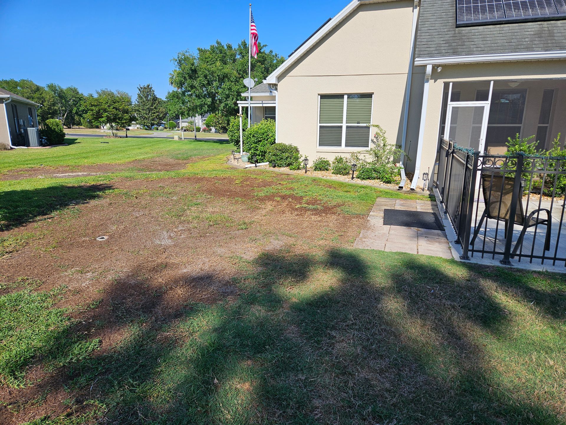 A house with patchy brown lawn and a sidewalk, flag in the background, sunny day.