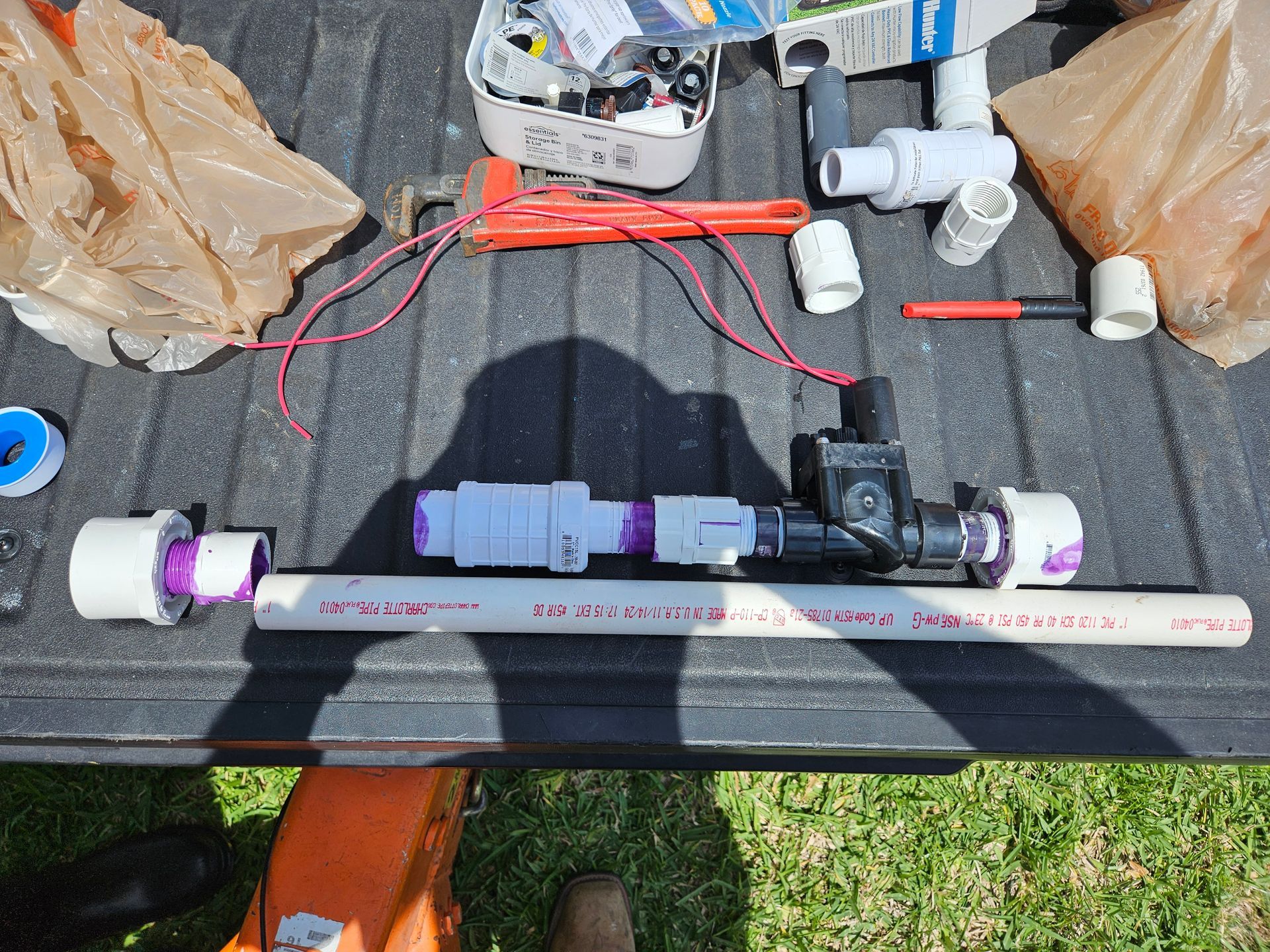 PVC pipe with sprinkler system parts, tools, and wiring on a truck bed.
