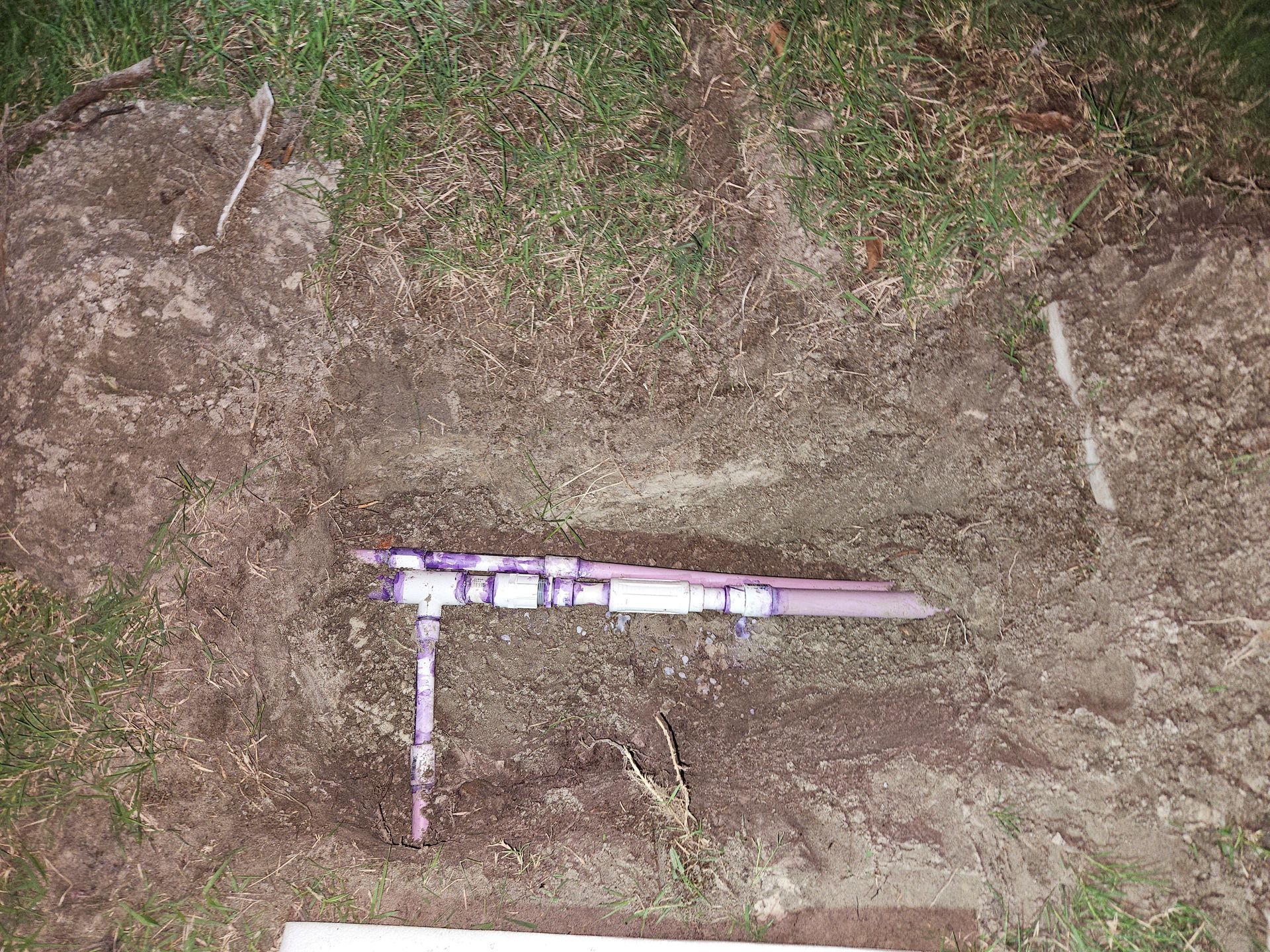 Pipes and fittings laid on dirt. A partly green lawn is nearby.