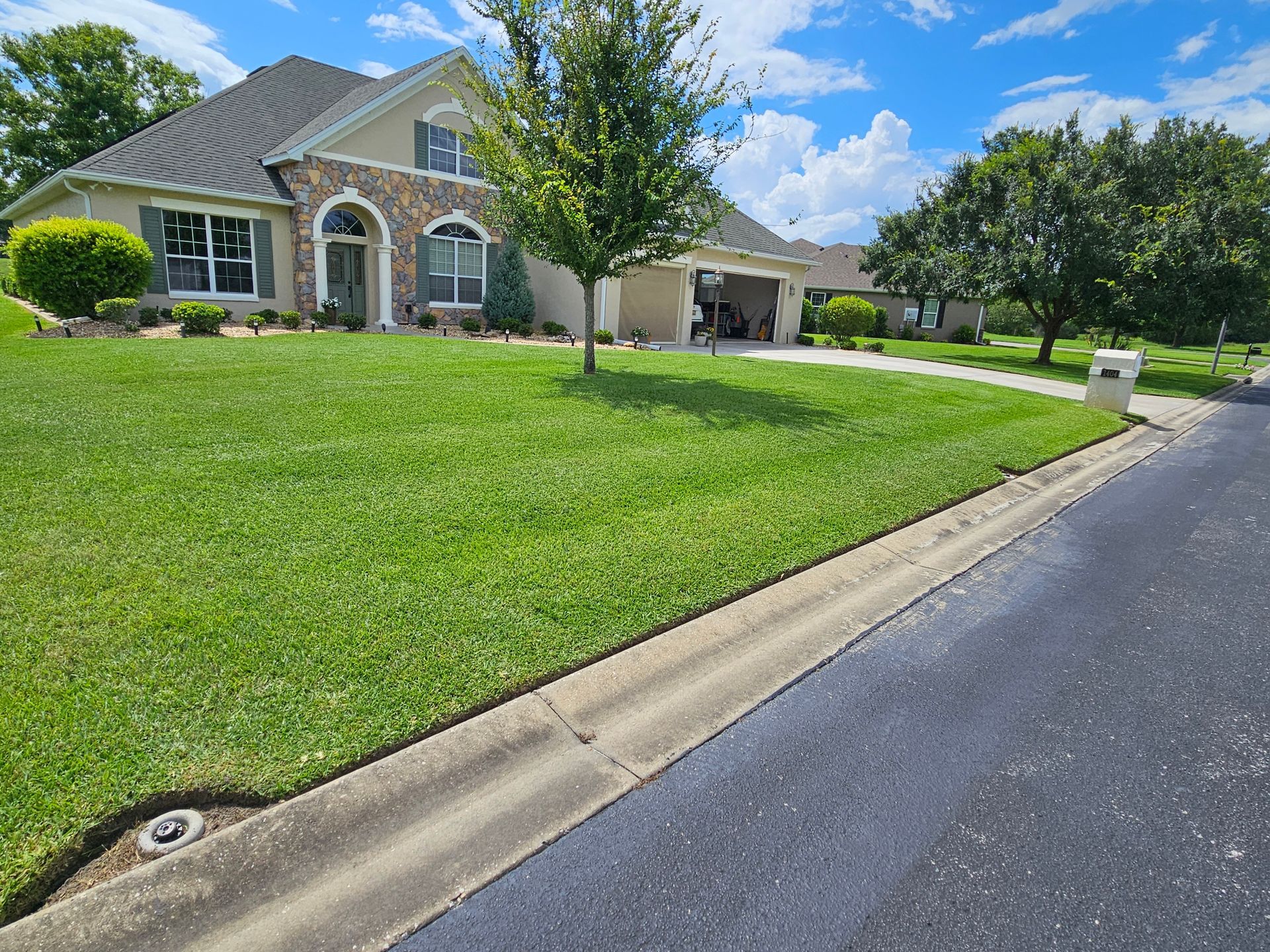 A house with green lawn and trees under a bright blue sky.