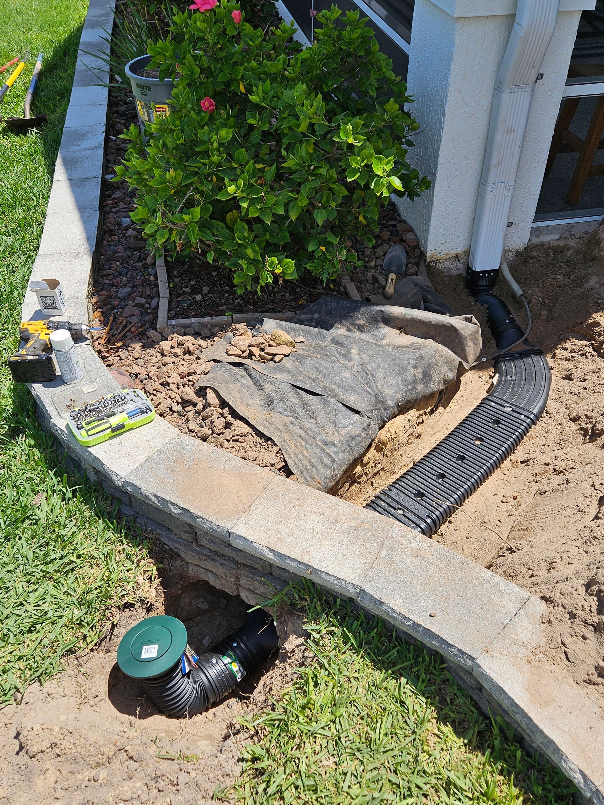 Landscaping project: flower bed with stone border, black drainage pipe, and fabric, next to white pillar.