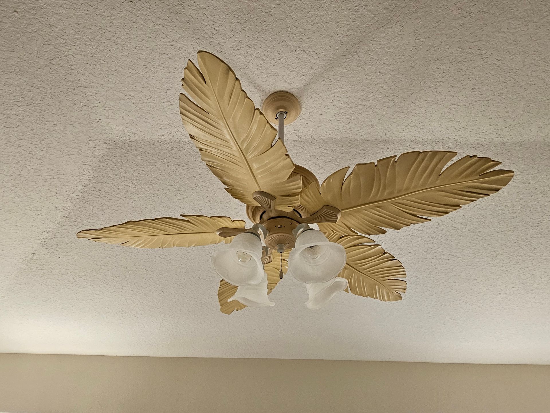 Ceiling fan with gold leaf-shaped blades and three frosted glass light fixtures, set against a textured white ceiling.
