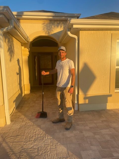 Man sweeping a paved area in front of a light-colored house.