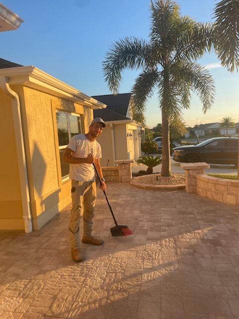 Man sweeping a patio in front of a house. Palm tree in the background. Sunny outdoors.