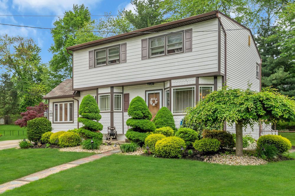 A white house with a lush green lawn and trees in front of it.