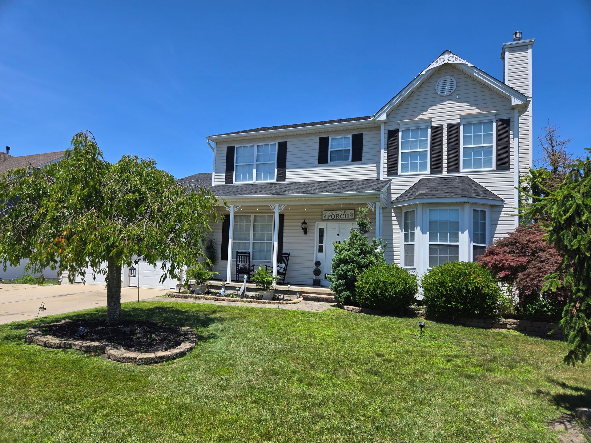 A large white house with black shutters is sitting on top of a lush green lawn.