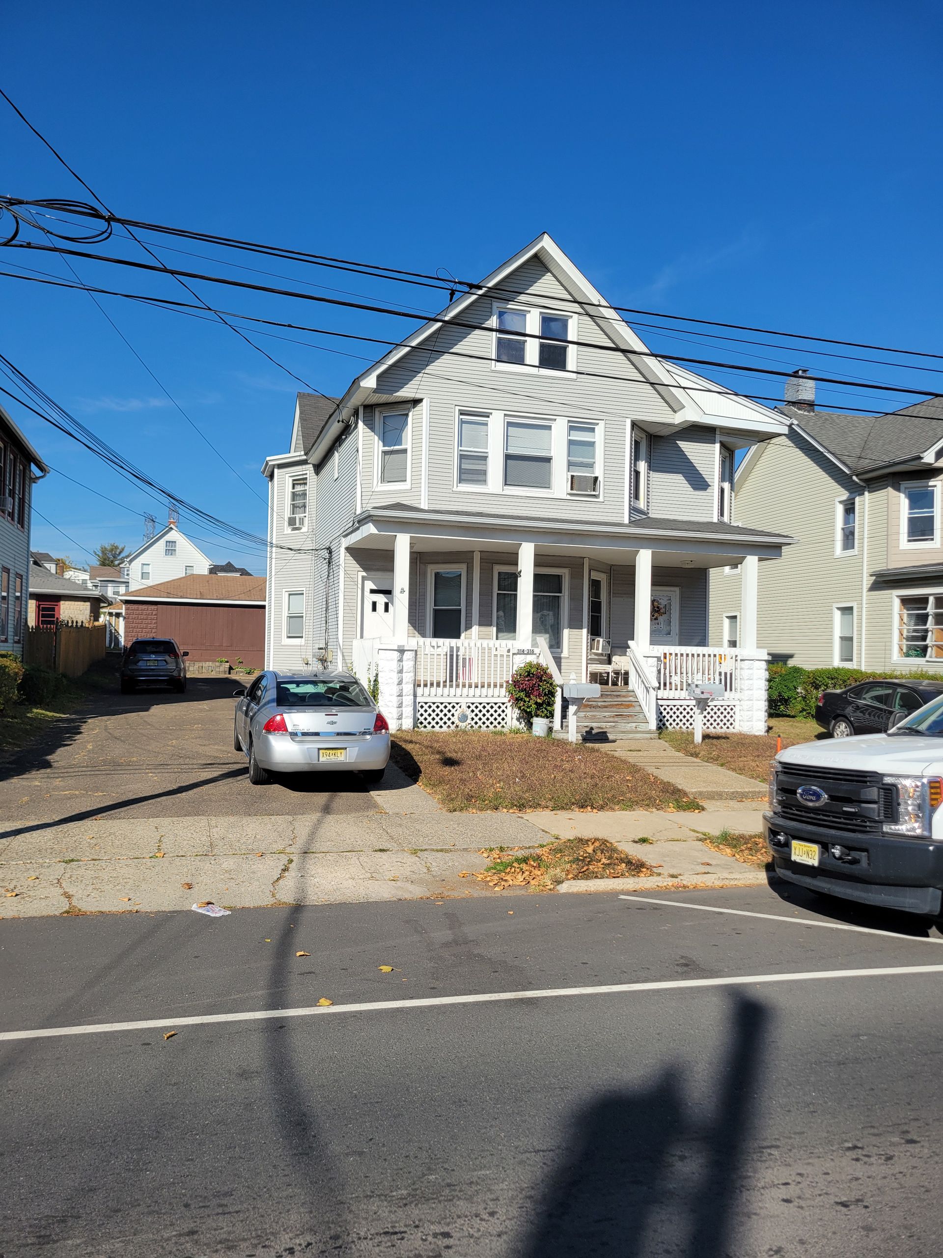 A recently sold white house in South Amboy with cars parked in front of it on a sunny day.
