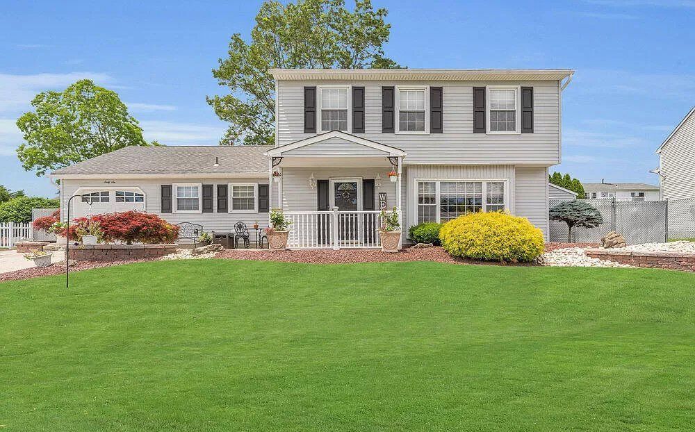 A white house with black shutters and a large lawn in front of it.