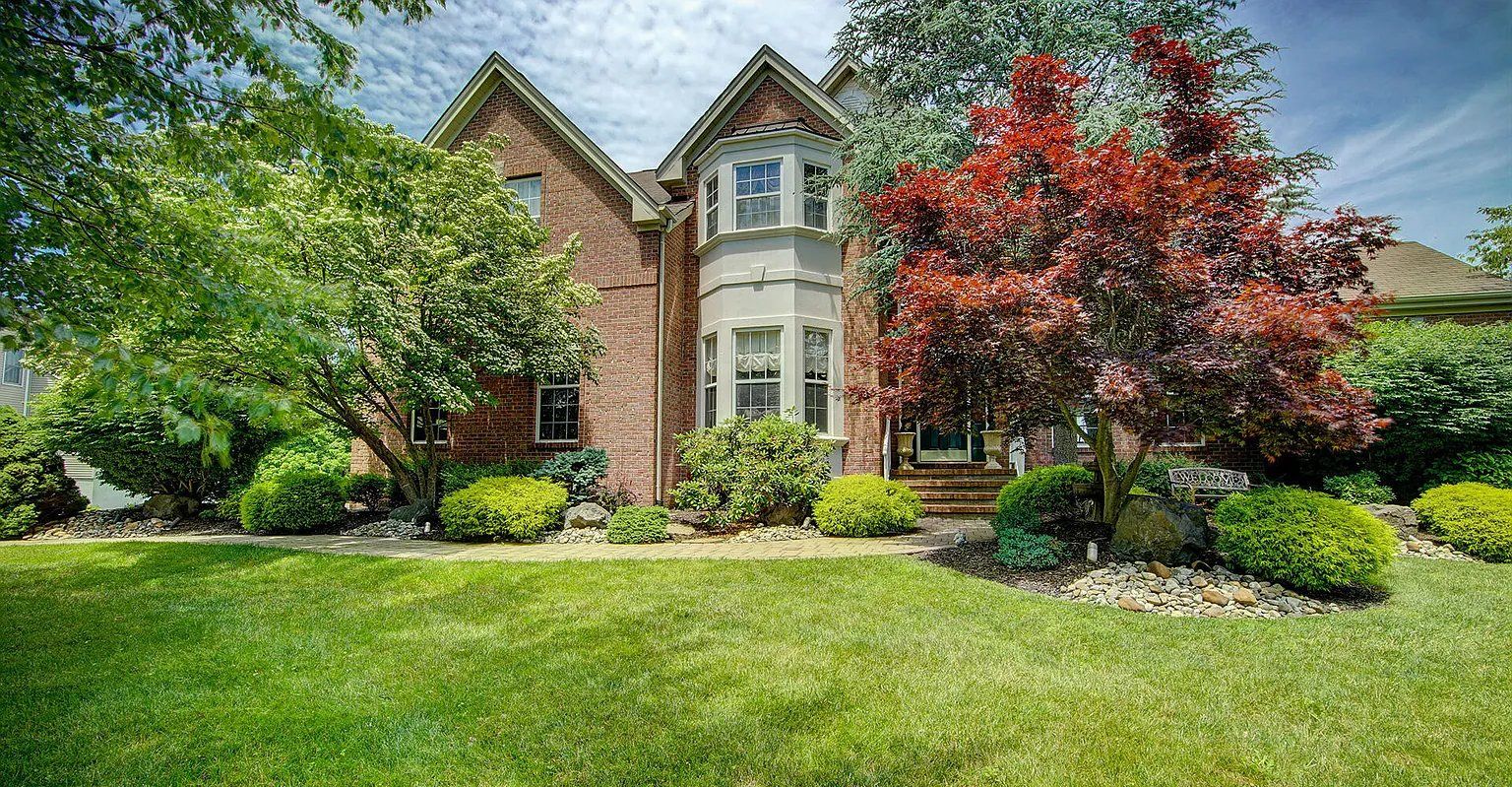 A large brick house with a lush green lawn and trees in front of it.