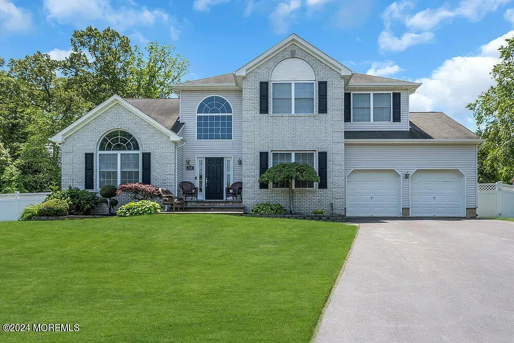 A large white brick house with black shutters and a large driveway.