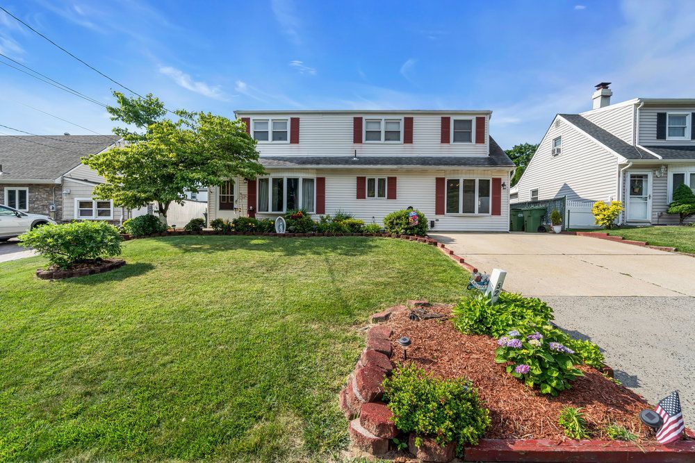 A large white house with red shutters is sitting on top of a lush green lawn.