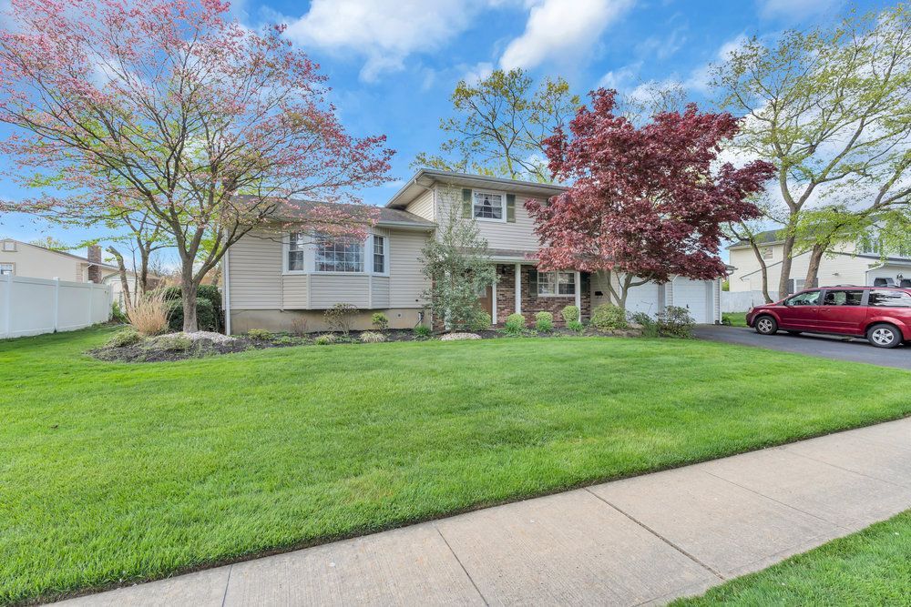 A house with a lush green lawn and a red car parked in front of it.