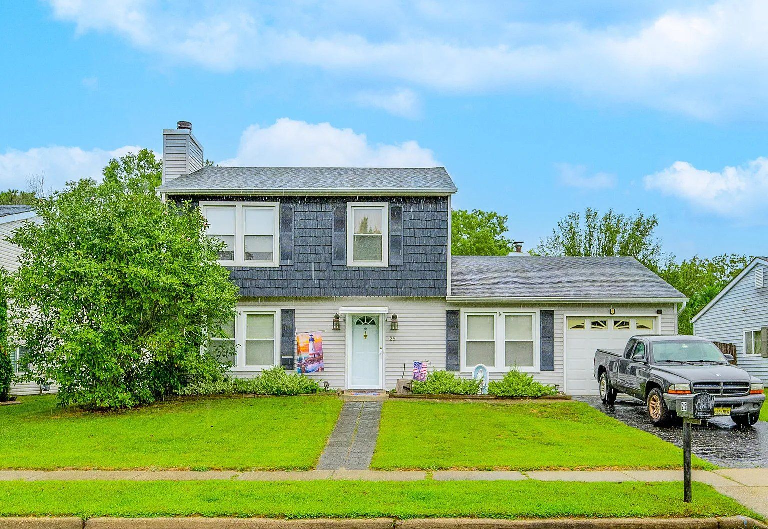 A white house with a black roof and a gray truck parked in front of it.
