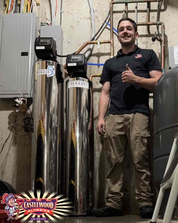 Man in work clothes gives thumbs up next to water filtration system. Basement setting.