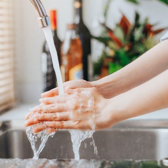 Hands being washed under running water in a kitchen sink.