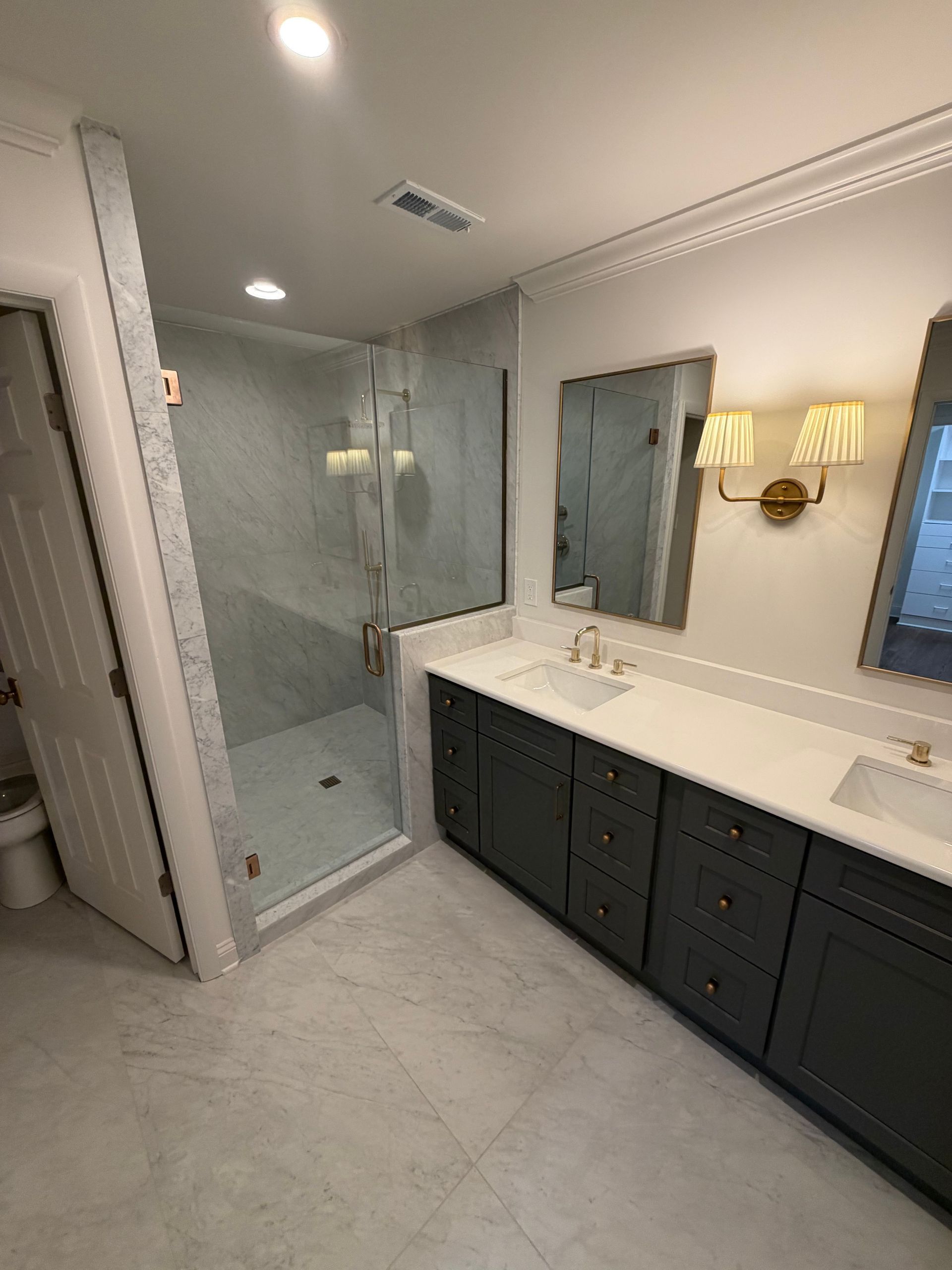 Modern bathroom with glass shower, double vanity, large mirror, and dark cabinets.