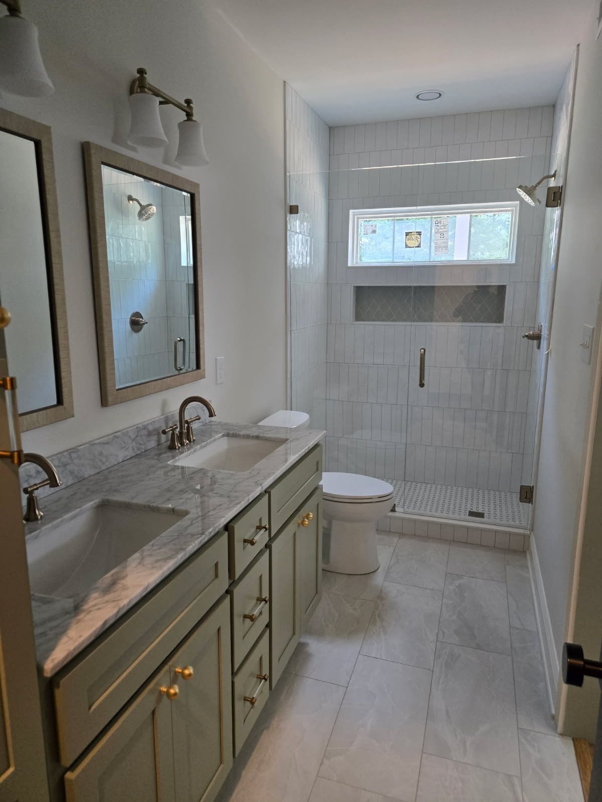 Narrow white bathroom with a vanity, mirror, sink, toilet, and tiled shower at the far end