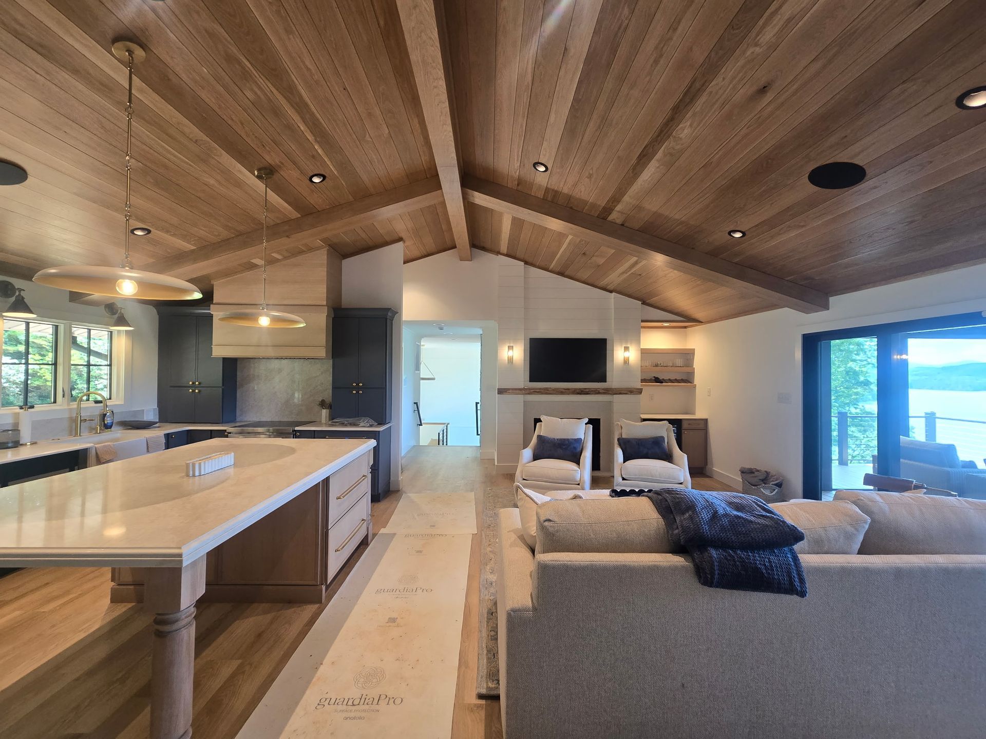 Modern open-plan living room and kitchen with wood ceiling, gray sofas, and large windows