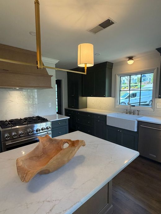 Modern kitchen with white island, black cabinets, stainless stove, and hanging light fixture