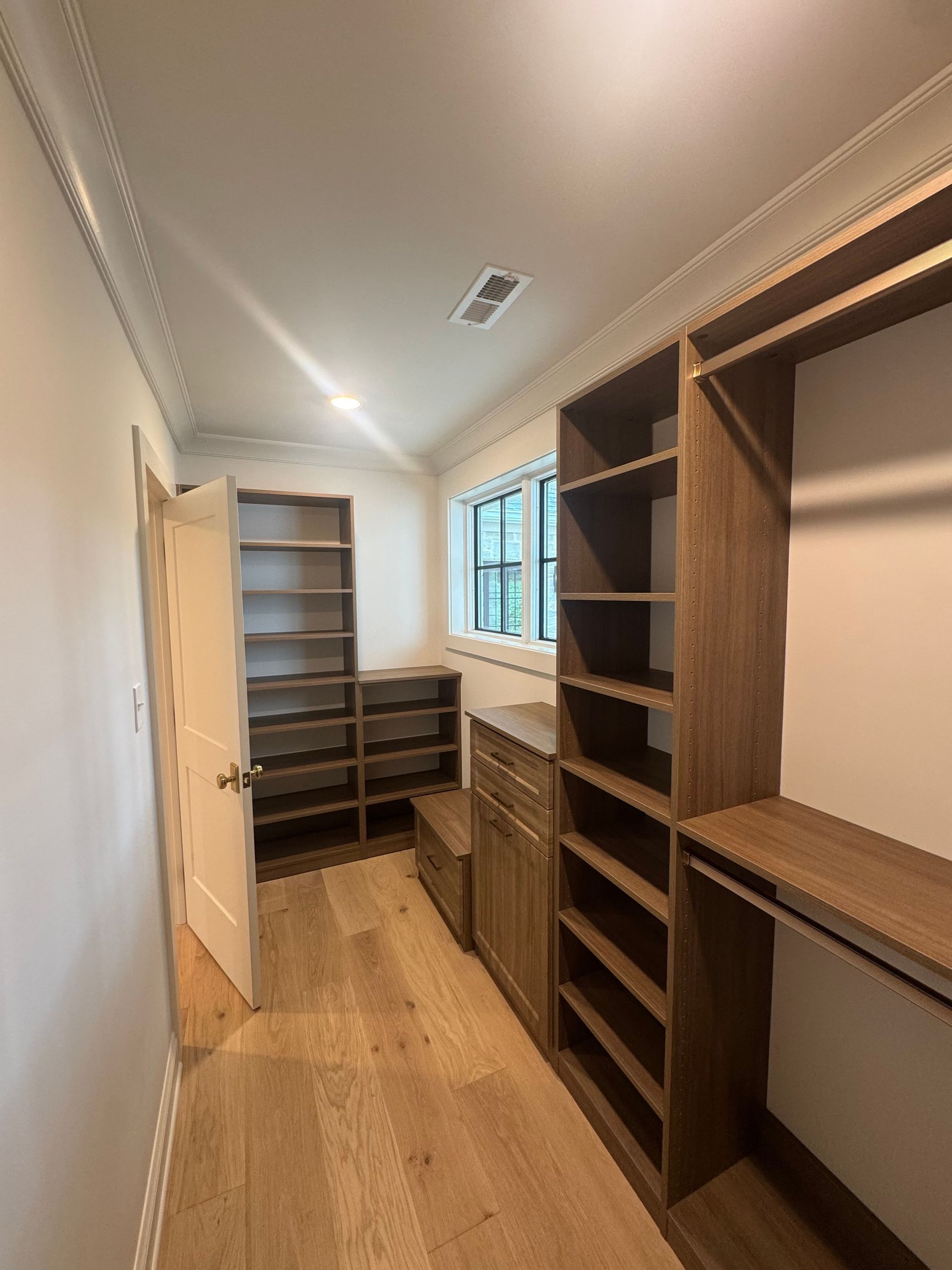 Empty walk-in closet with built-in wooden shelves, drawers, and hanging rods along a narrow hallway.