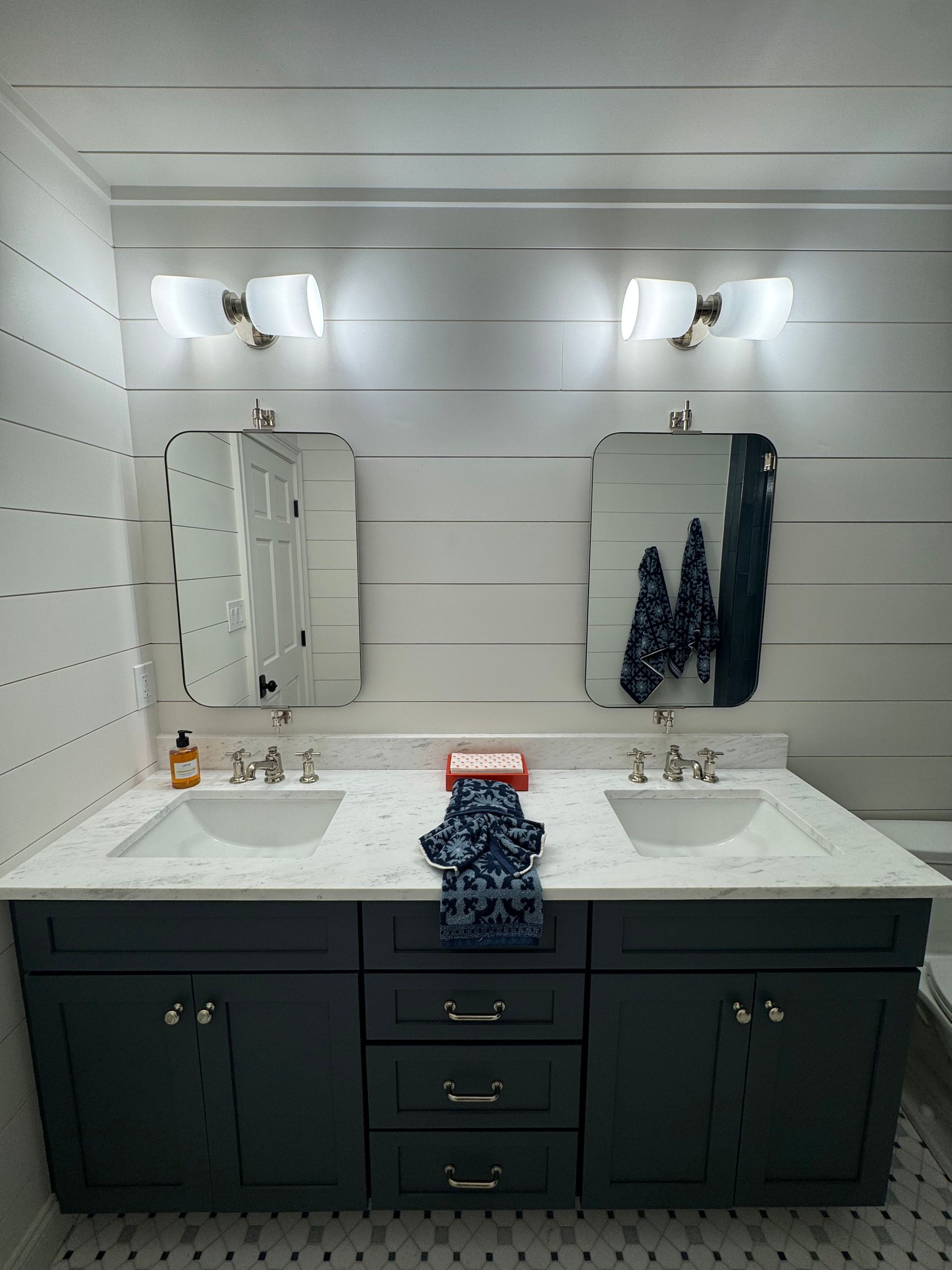Double vanity bathroom with white sinks, black cabinet, mirrors, and wall sconces