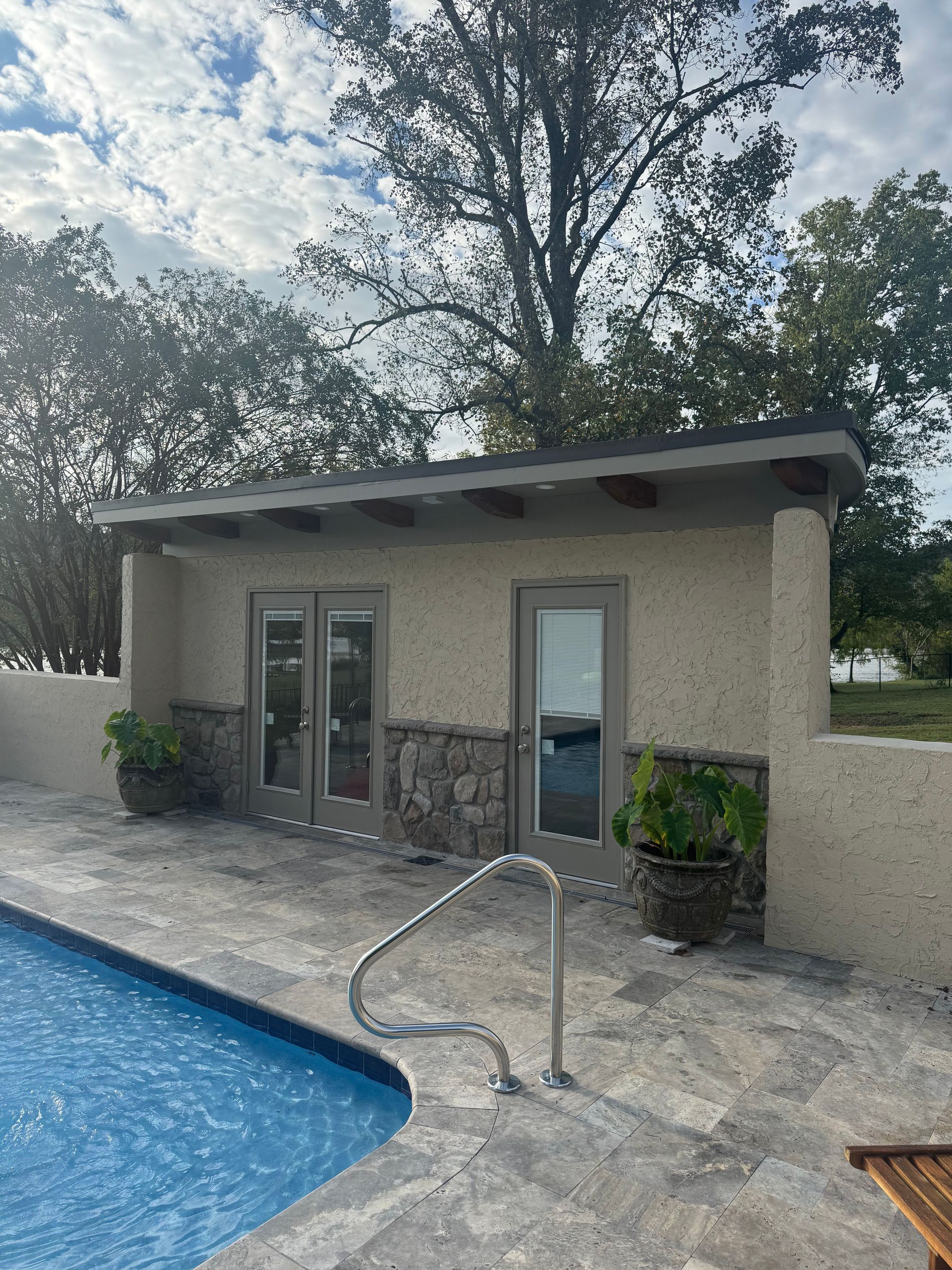 Poolside patio with a small building, glass doors, and a metal handrail beside the water