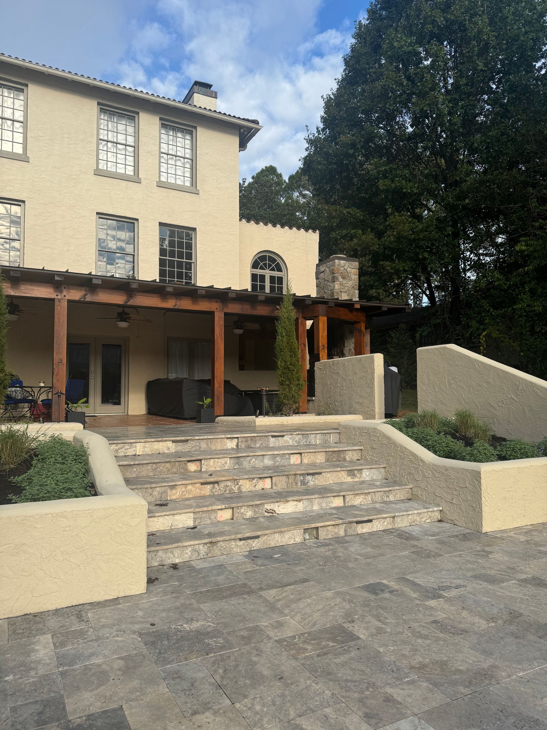 Stone steps lead to a tan stucco building with a wooden porch and trees beside it.