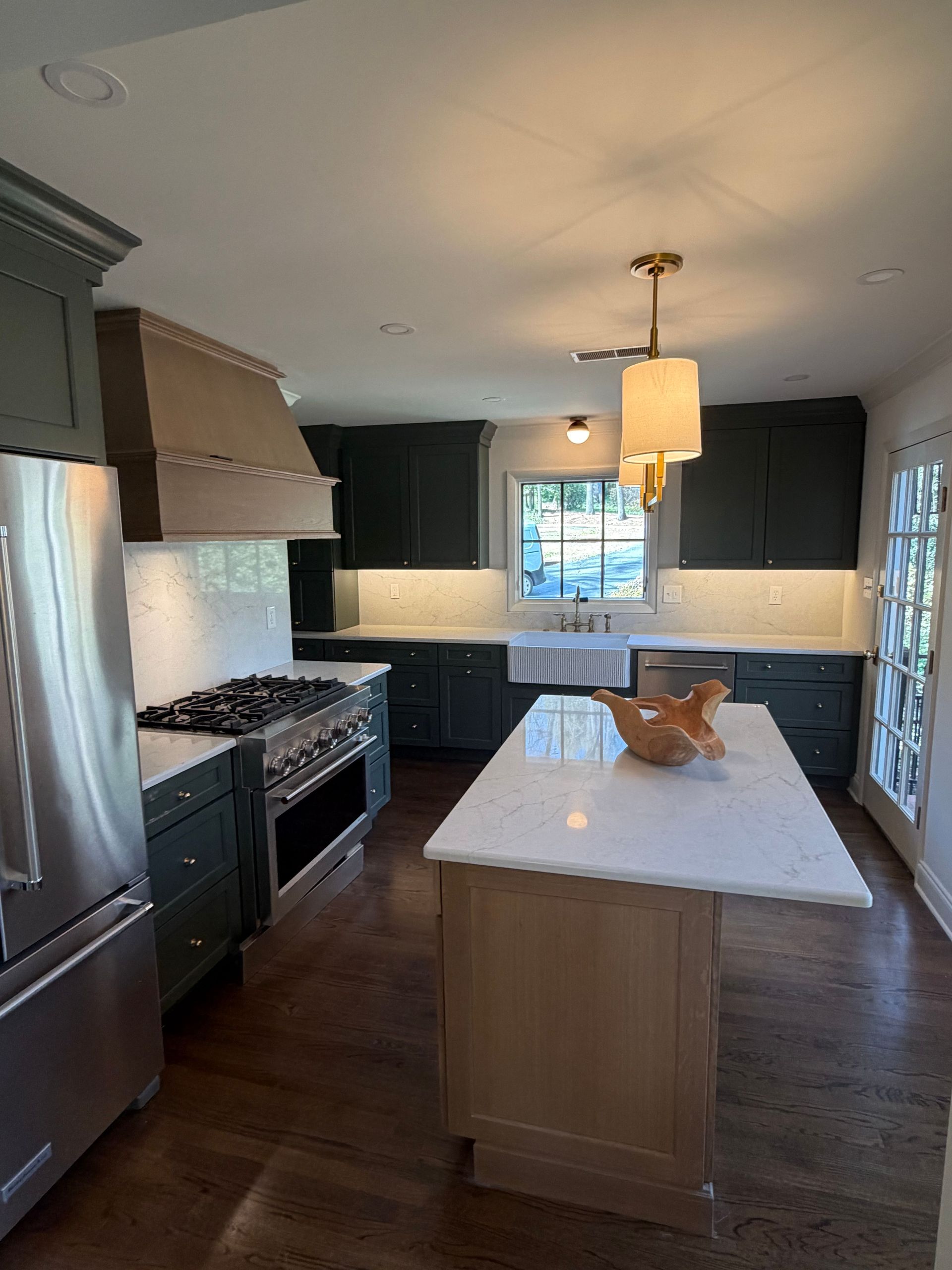 Modern kitchen with island, stainless stove, white countertops, dark cabinets, and a window above the sink.