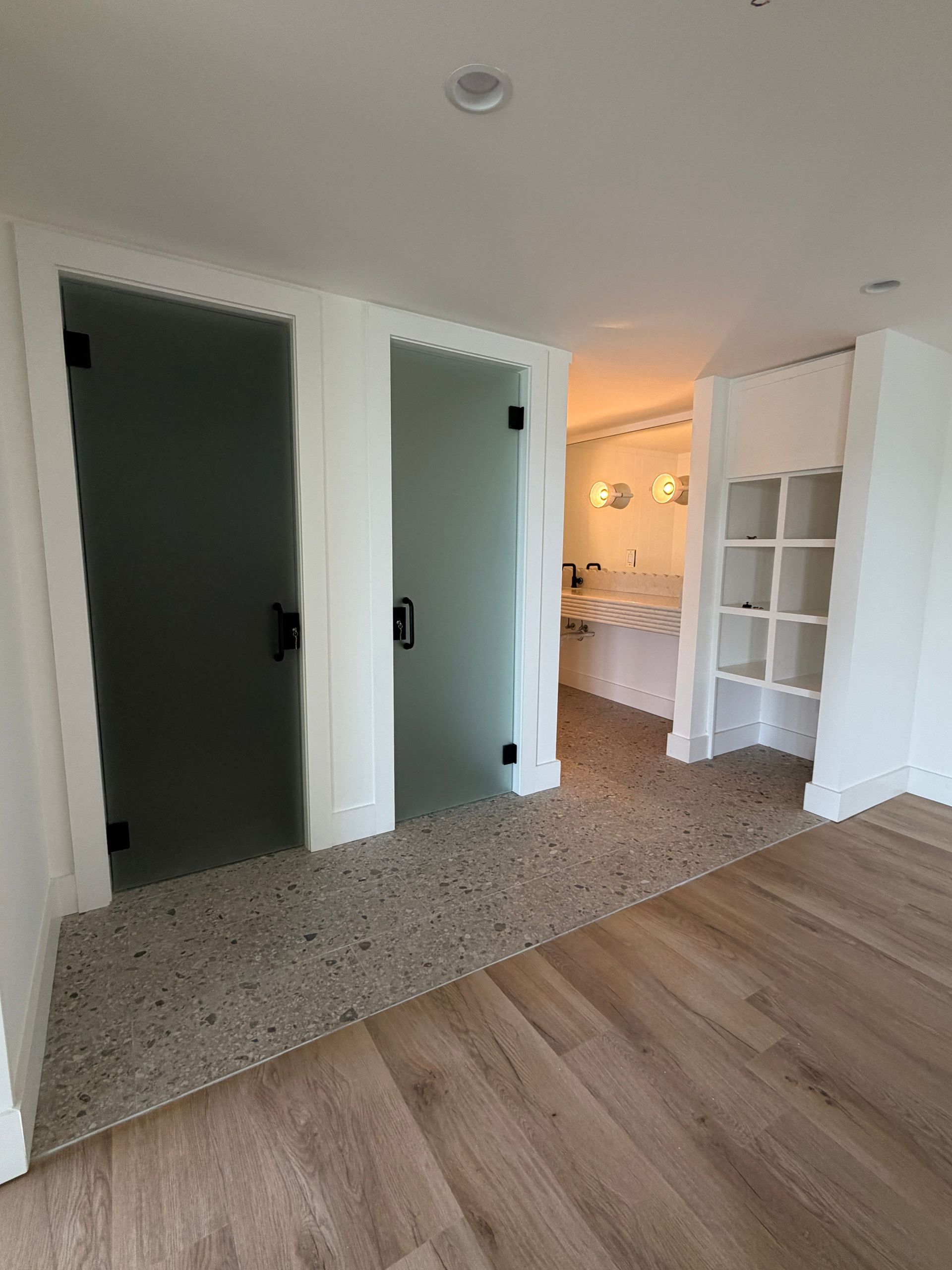 Modern hallway with green double doors, wood floor, and a lit room in the background