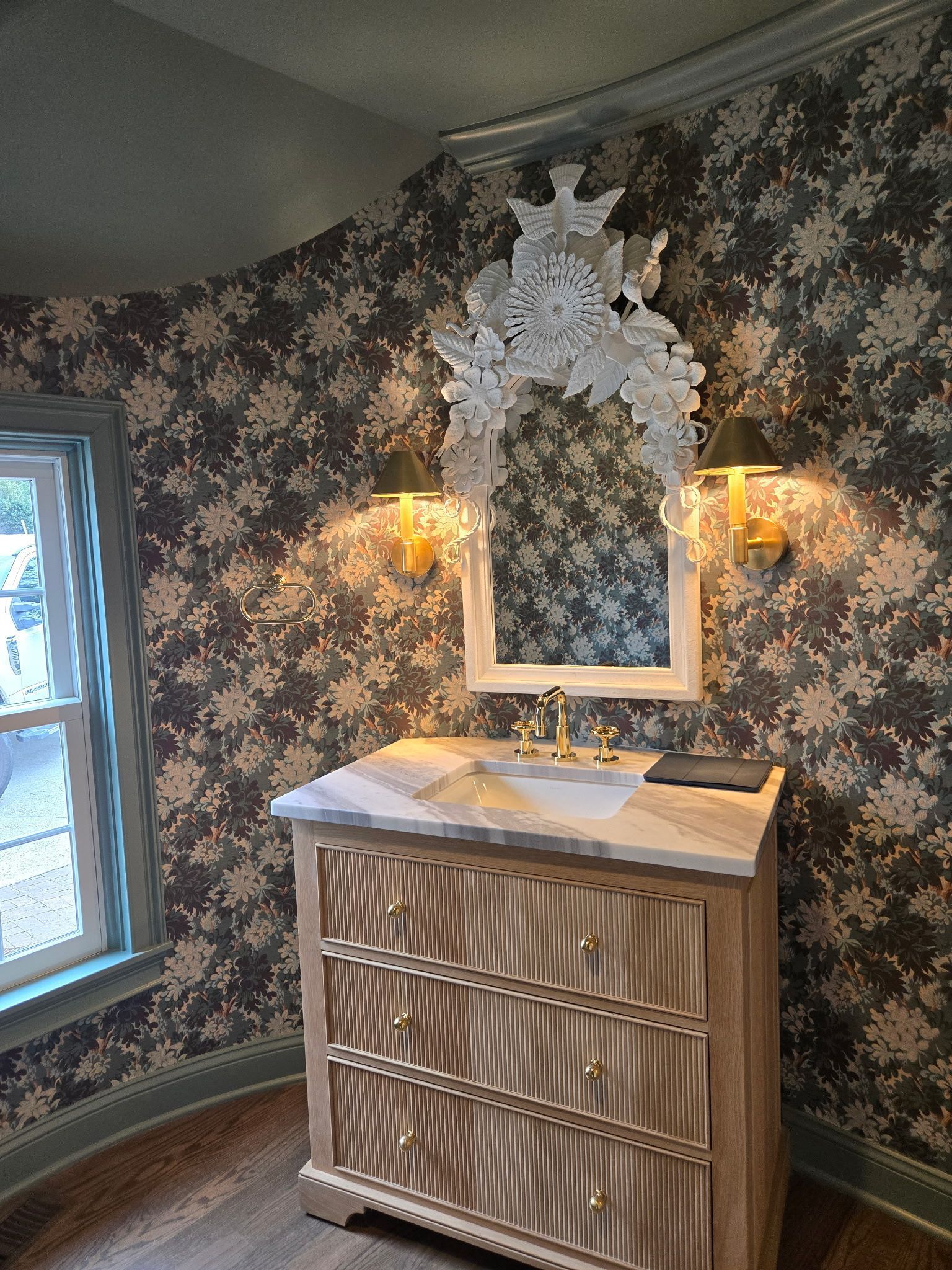 Ornate mirrored dresser with wall sconces and floral wallpaper in a vintage-style room