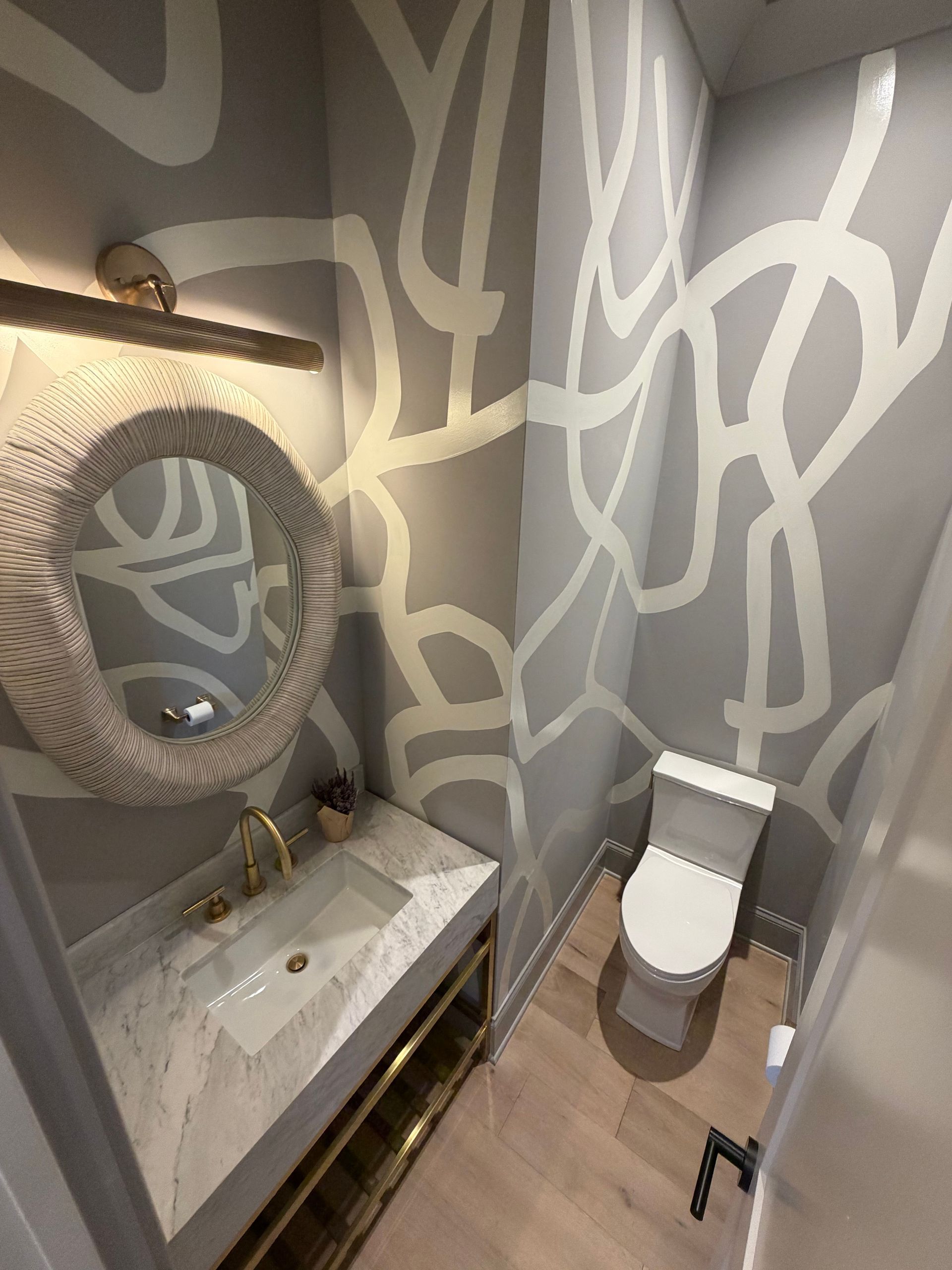 Small modern bathroom with patterned gray walls, sink, round mirror, and toilet.
