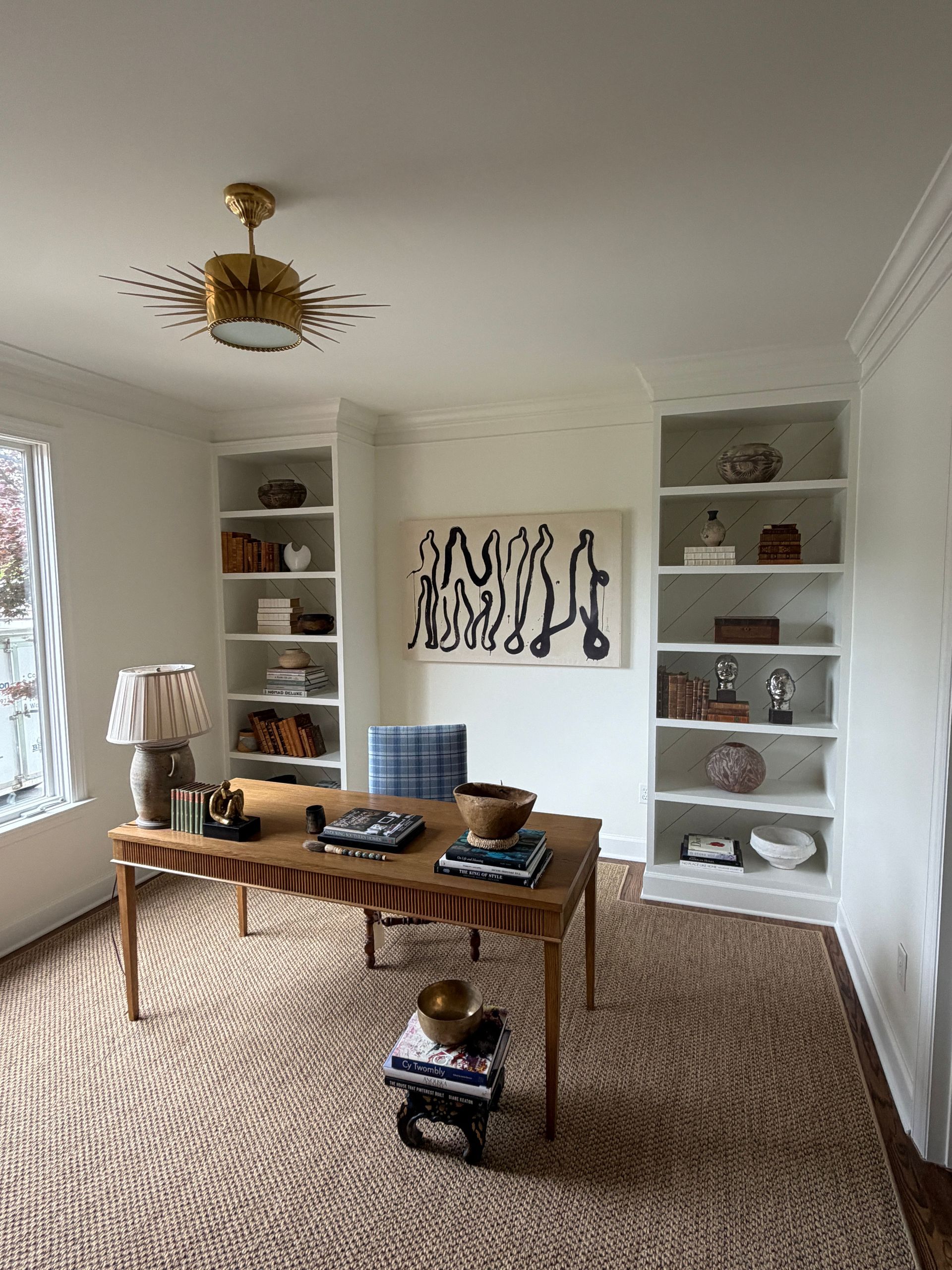 Bright living room with dining table, built-in shelves, artwork, and woven rug in neutral tones