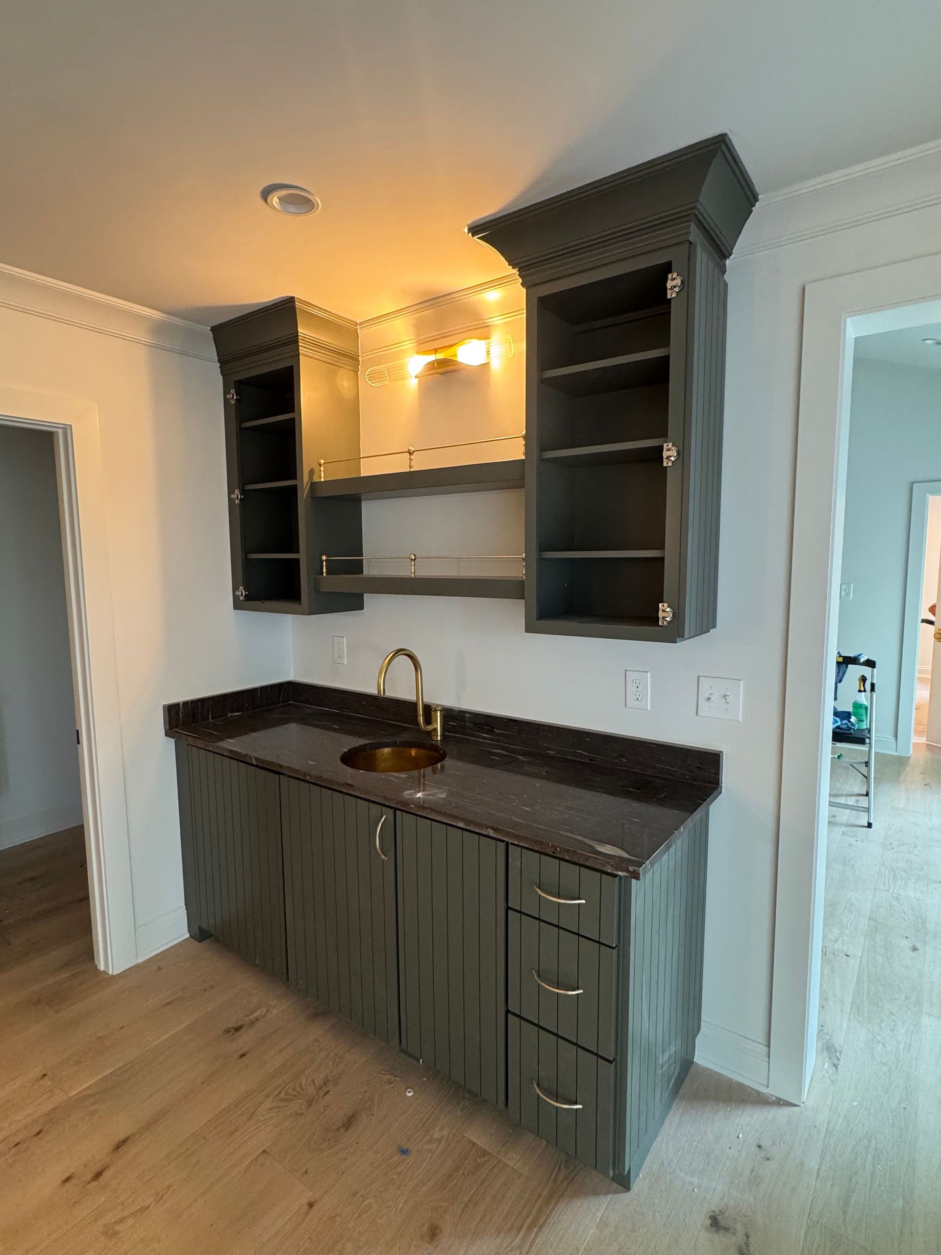 Small kitchen nook with dark cabinets, black countertop, sink, and open shelving on a light wood floor