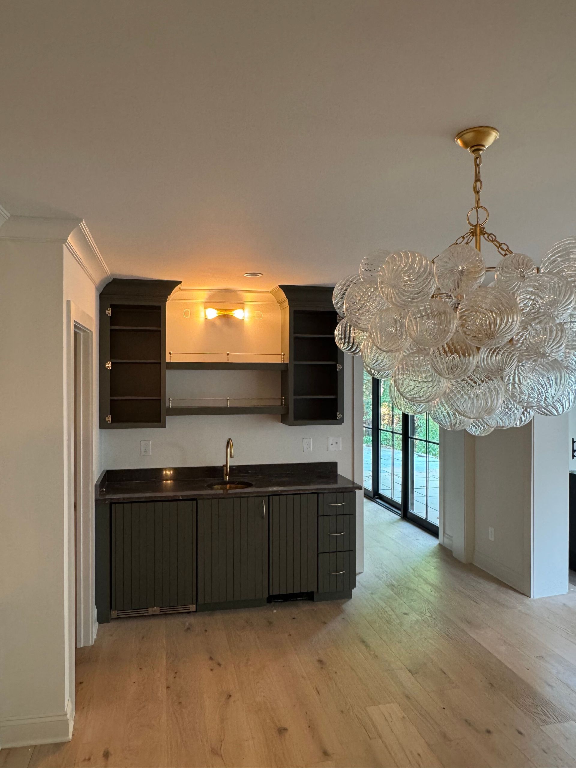 Modern kitchen with dark cabinets, light wood floors, and a crystal chandelier in an open room