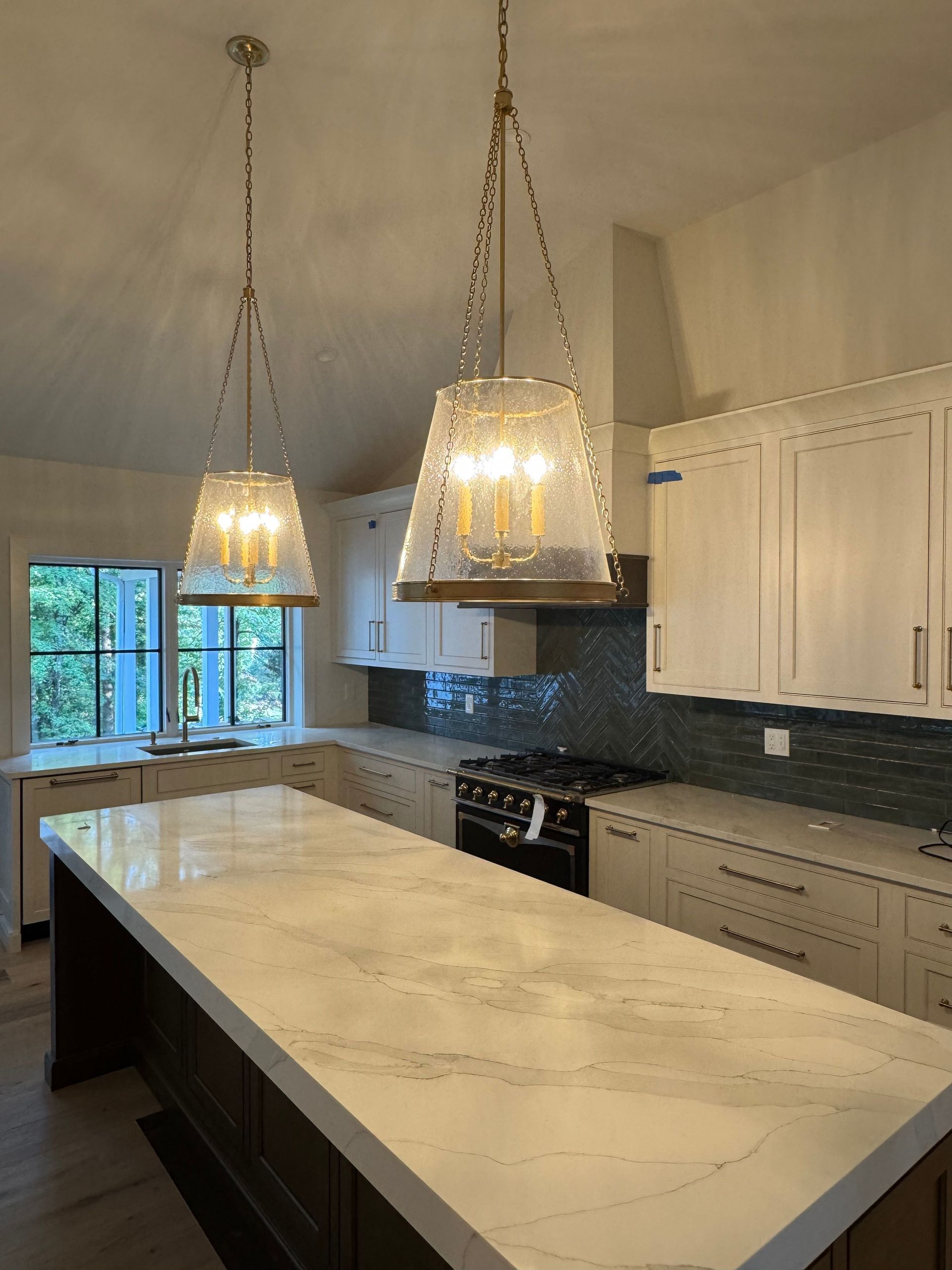 Modern kitchen with large marble island, white cabinets, and two hanging pendant lights.