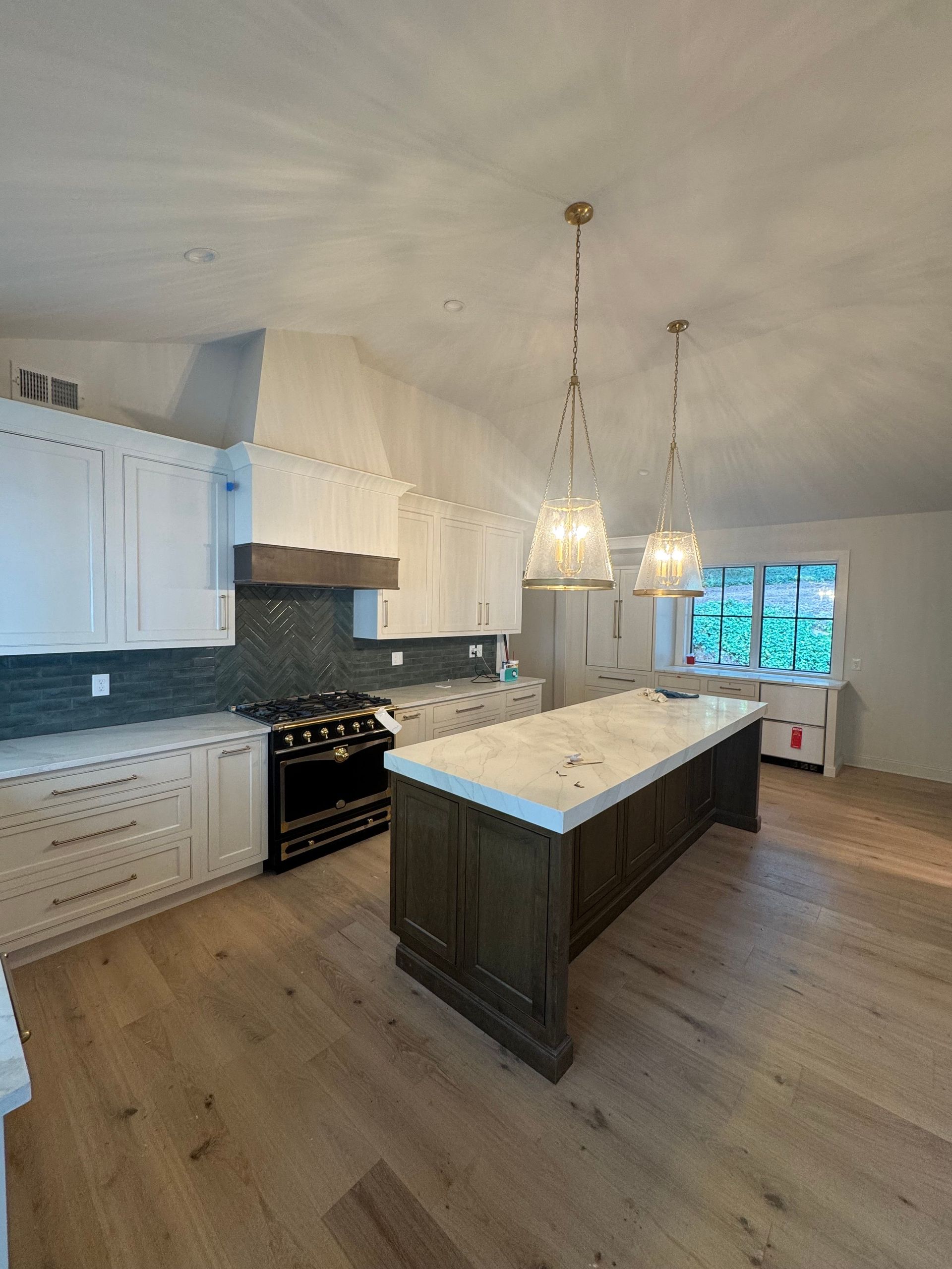 Modern kitchen with white cabinets, dark island, pendant lights, and a black stove by a window.