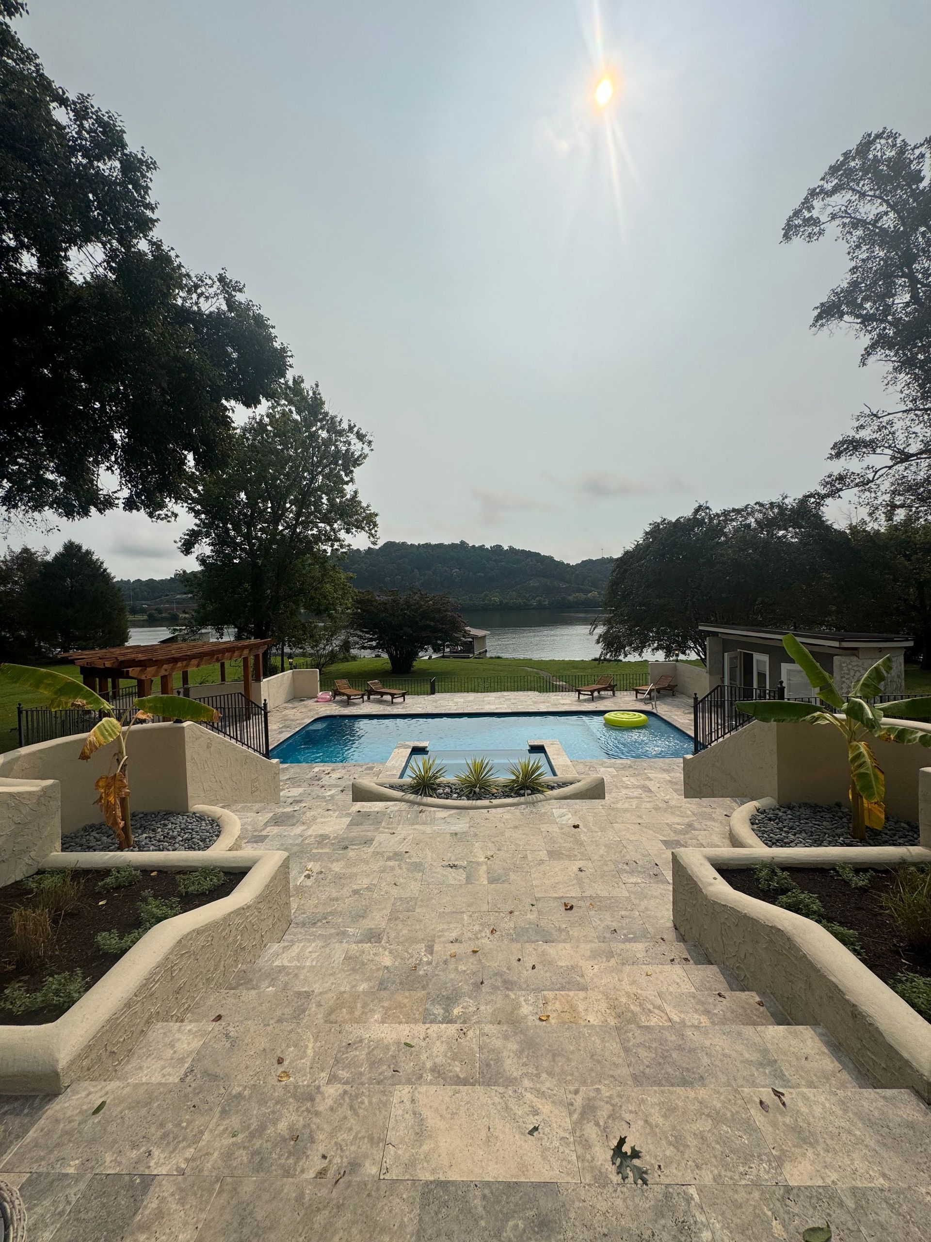 Stone steps lead to a resort pool overlooking a lake under a bright sky.