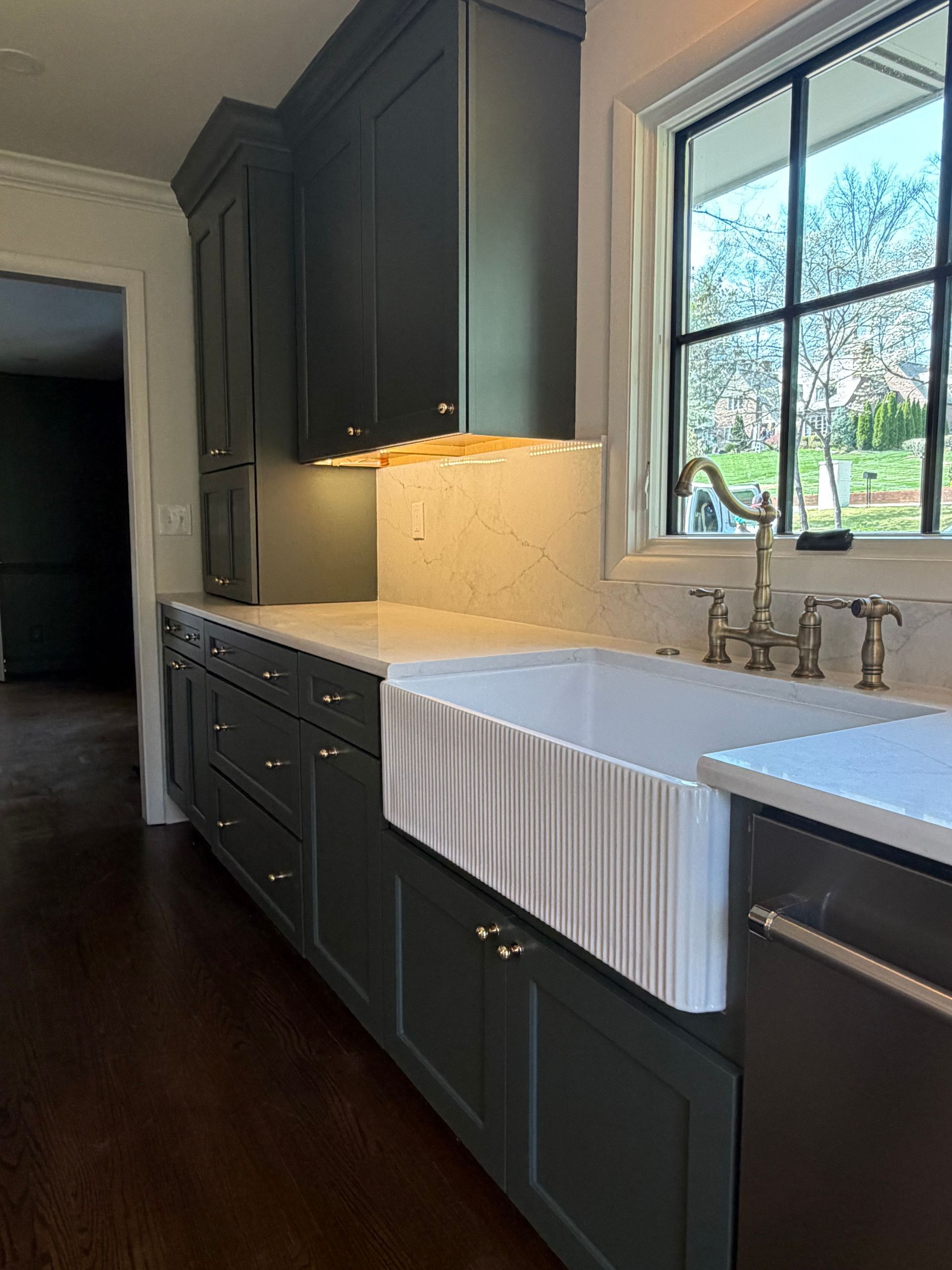 Modern kitchen with dark cabinets, white countertops, a farmhouse sink, and a large window.