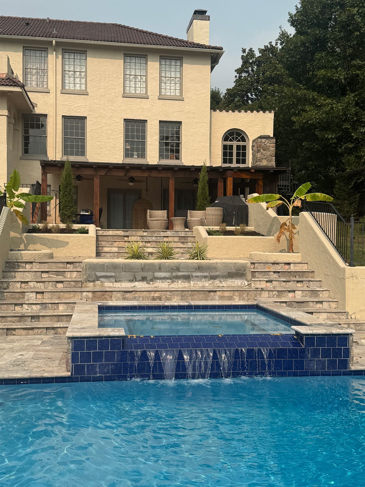 Luxury house with stone steps, terrace, and blue swimming pool in a landscaped backyard.