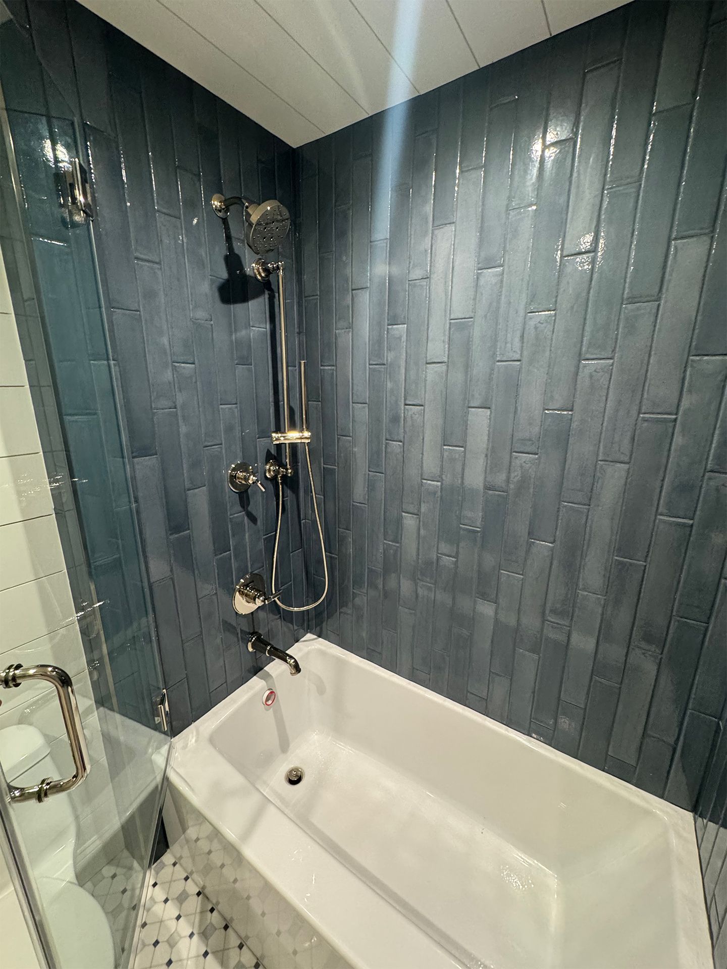 Small tiled bathroom shower and tub with dark blue walls and a black shower fixture.