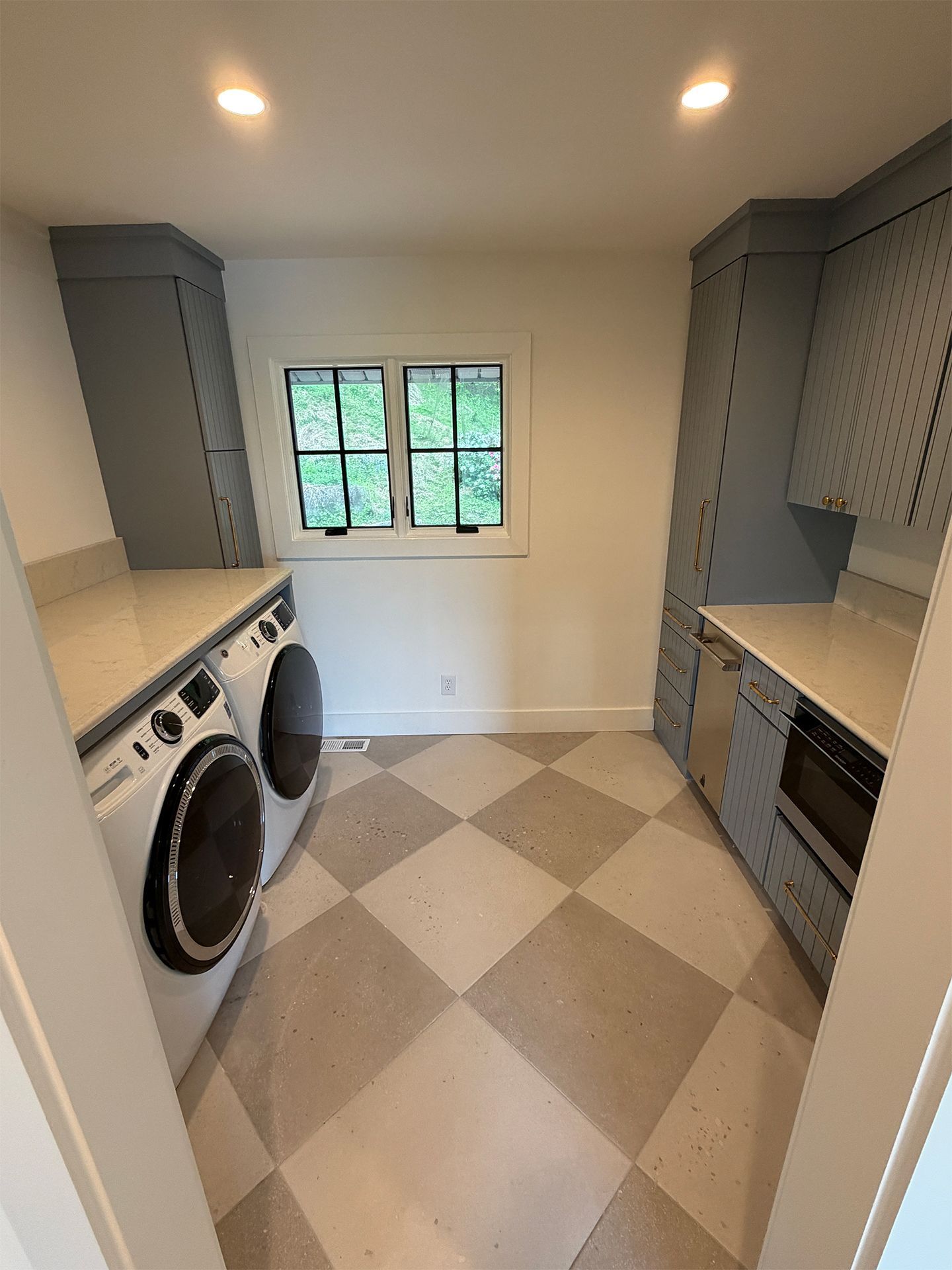 Small laundry room with gray cabinets, checkerboard floor, washer, dryer, and a window.