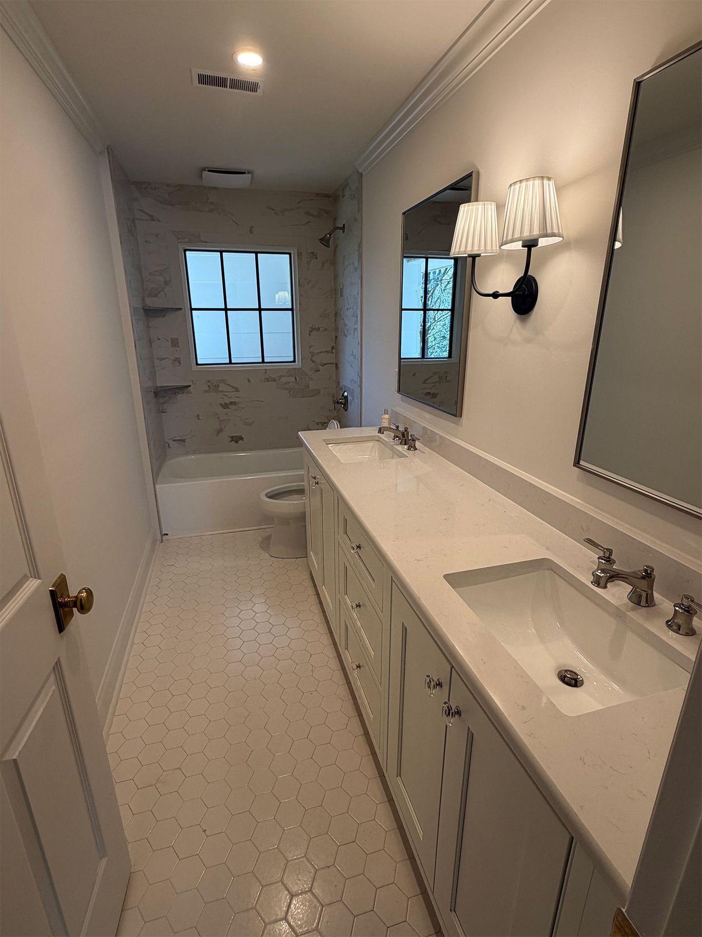 Bright white bathroom with vanity, sink, mirror, wall sconces, and a tub at the far end.